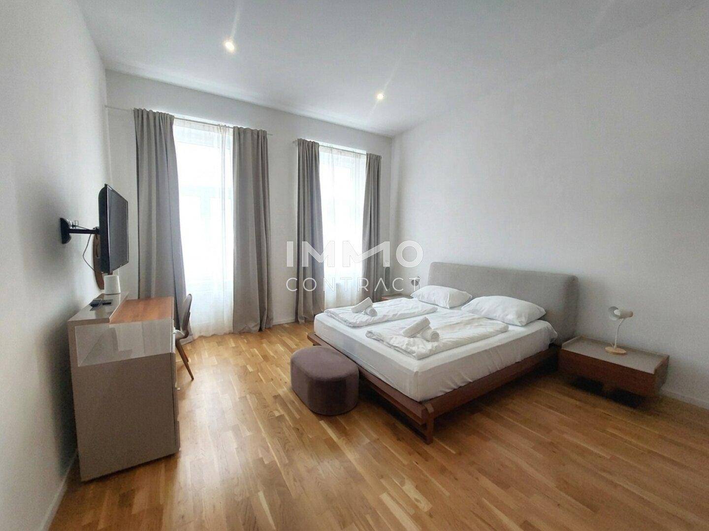 Geräumiges Schlafzimmer mit Doppelbett, Schreibtisch und Fernseher, hell durch große Fenster.