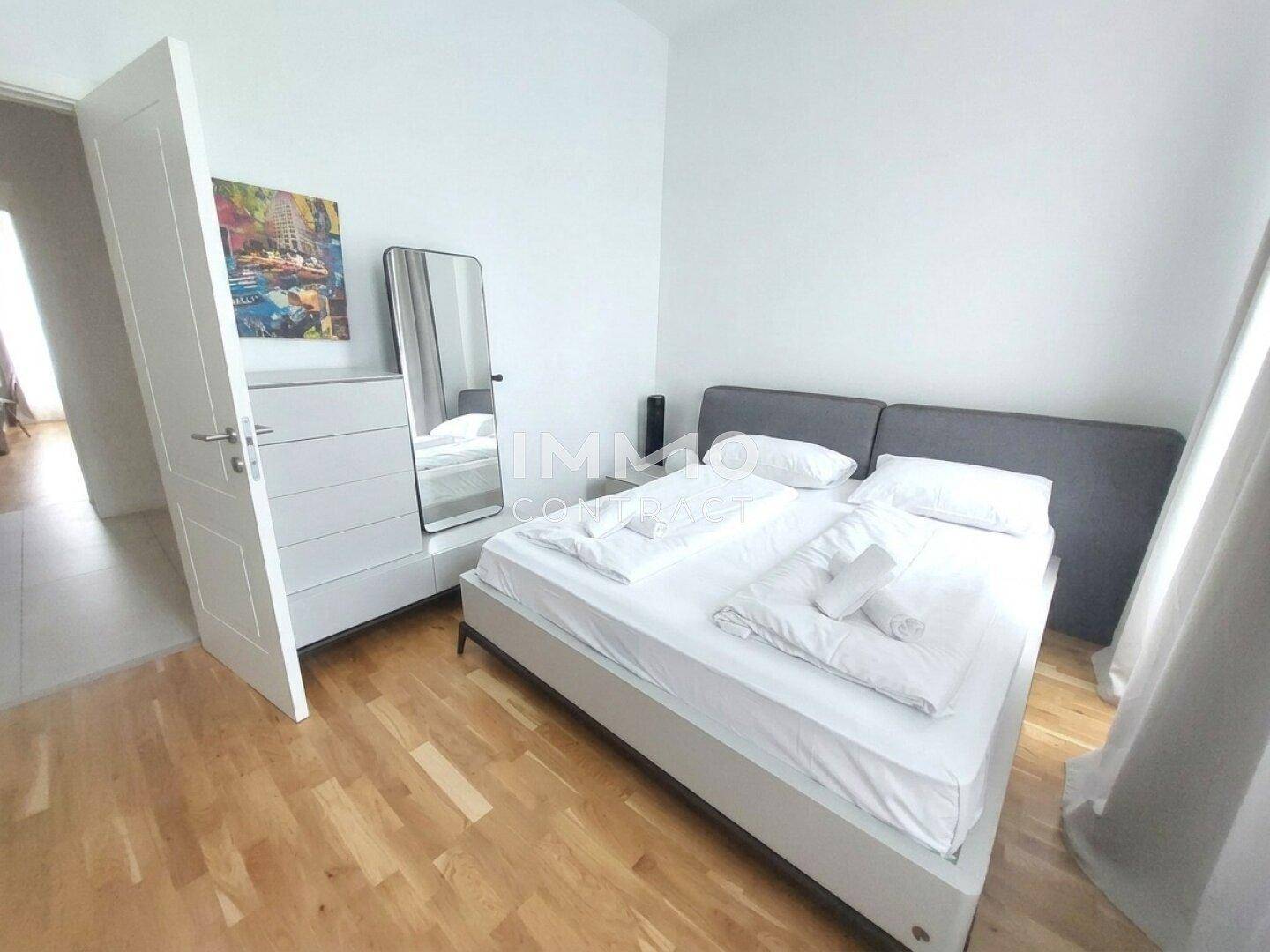 Modernes Schlafzimmer mit Holzboden, Kommode und Spiegel, bietet eine helle und freundliche Atmosphäre.