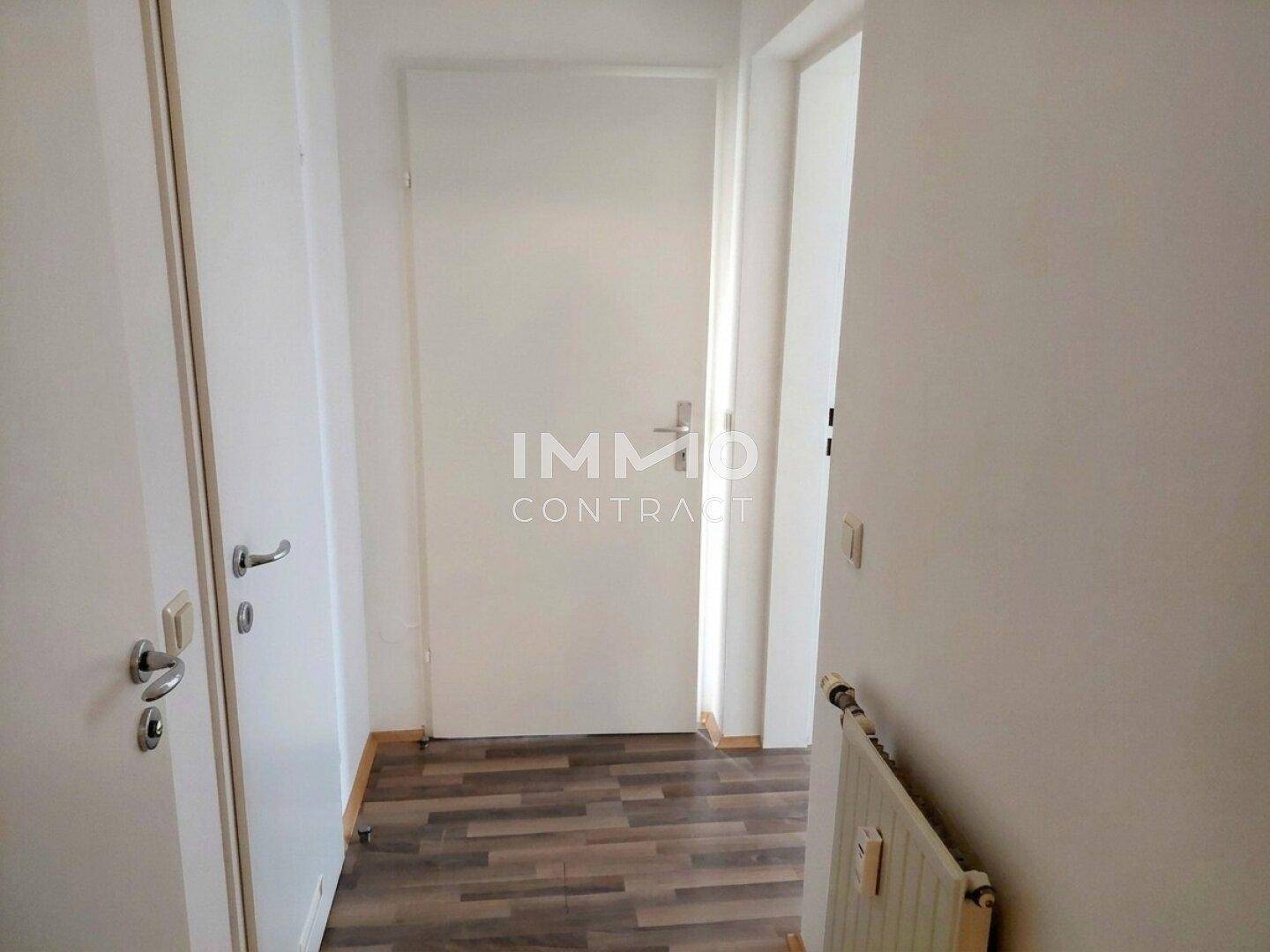 Heller Flur mit Laminatboden, weißen Türen und einem Heizkörper.