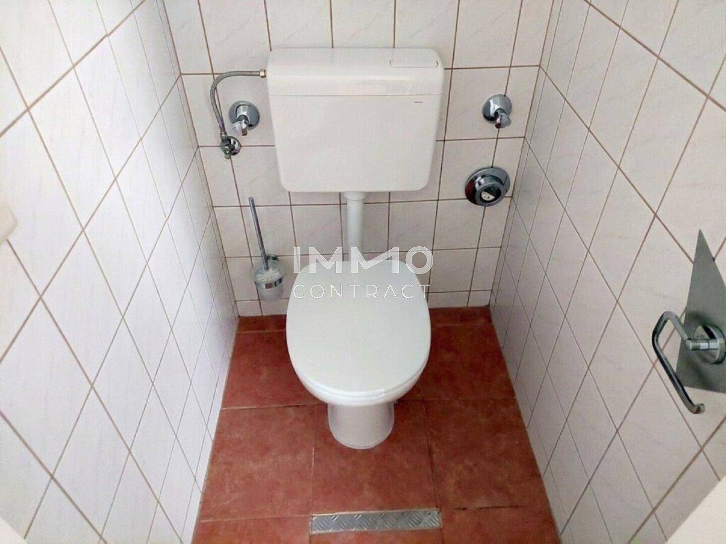 Separate Toilette mit weißen Wandfliesen und terrakottafarbenem Boden.