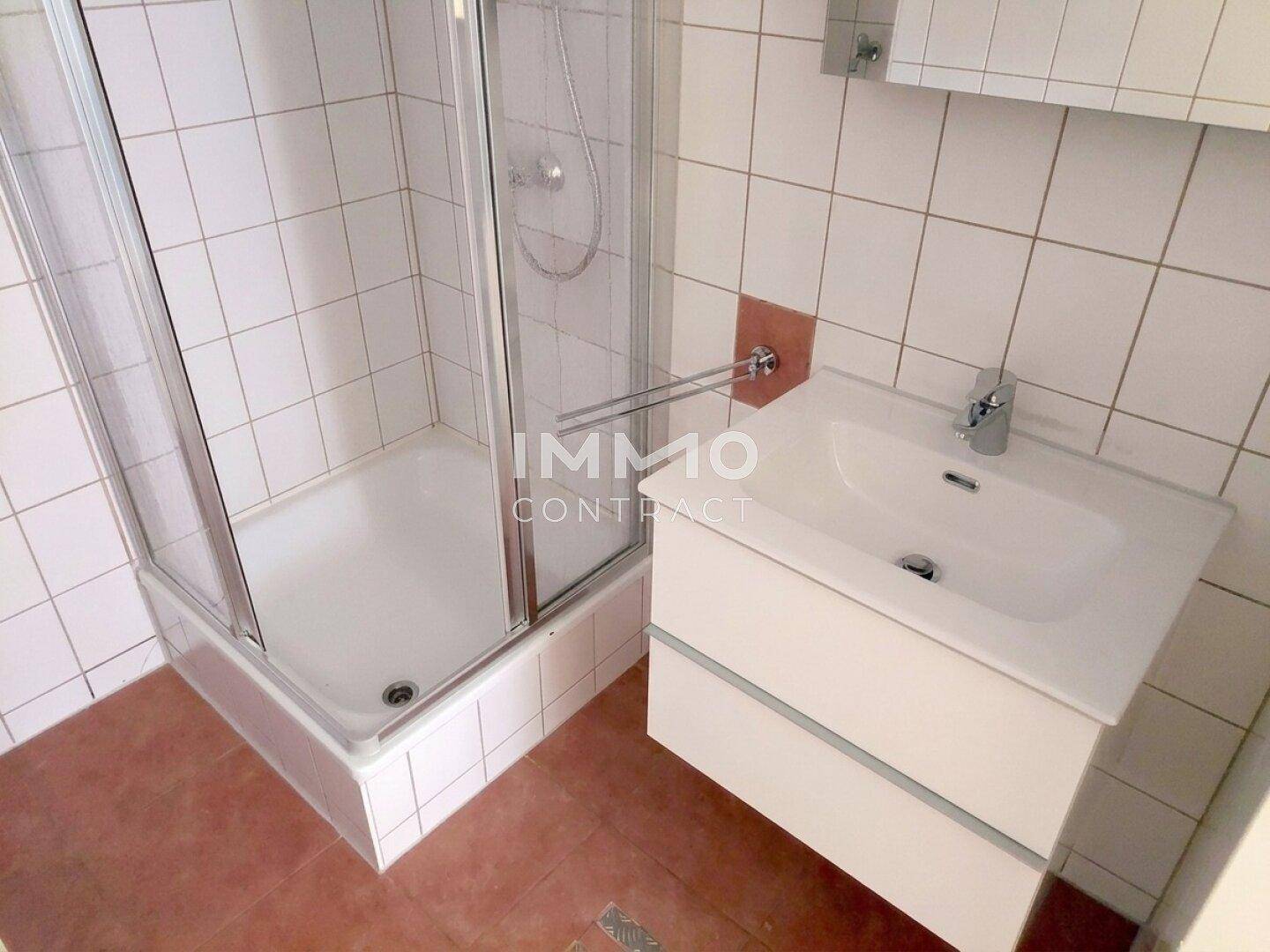 Badezimmer mit Duschkabine, Waschbeckenunterschrank und hellen Fliesen.