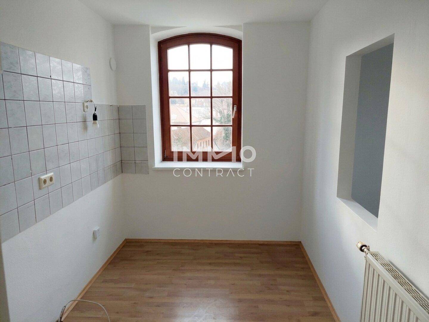Leere Küche mit Laminatboden, gefliester Wand und einem großen Rundbogenfenster.