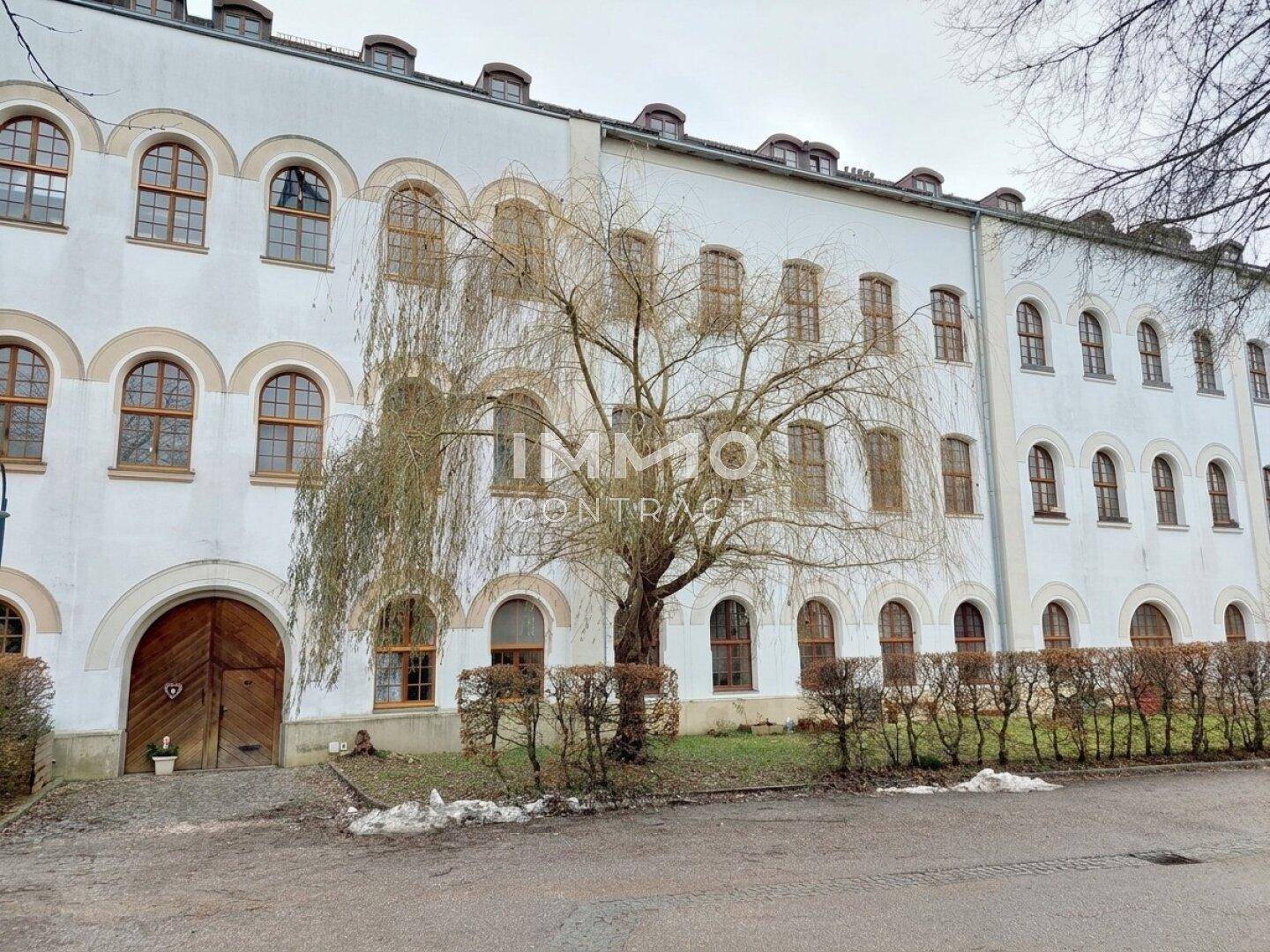 Historische Fassade eines Gebäudes mit vielen Rundbogenfenstern und einem großen Holztor.