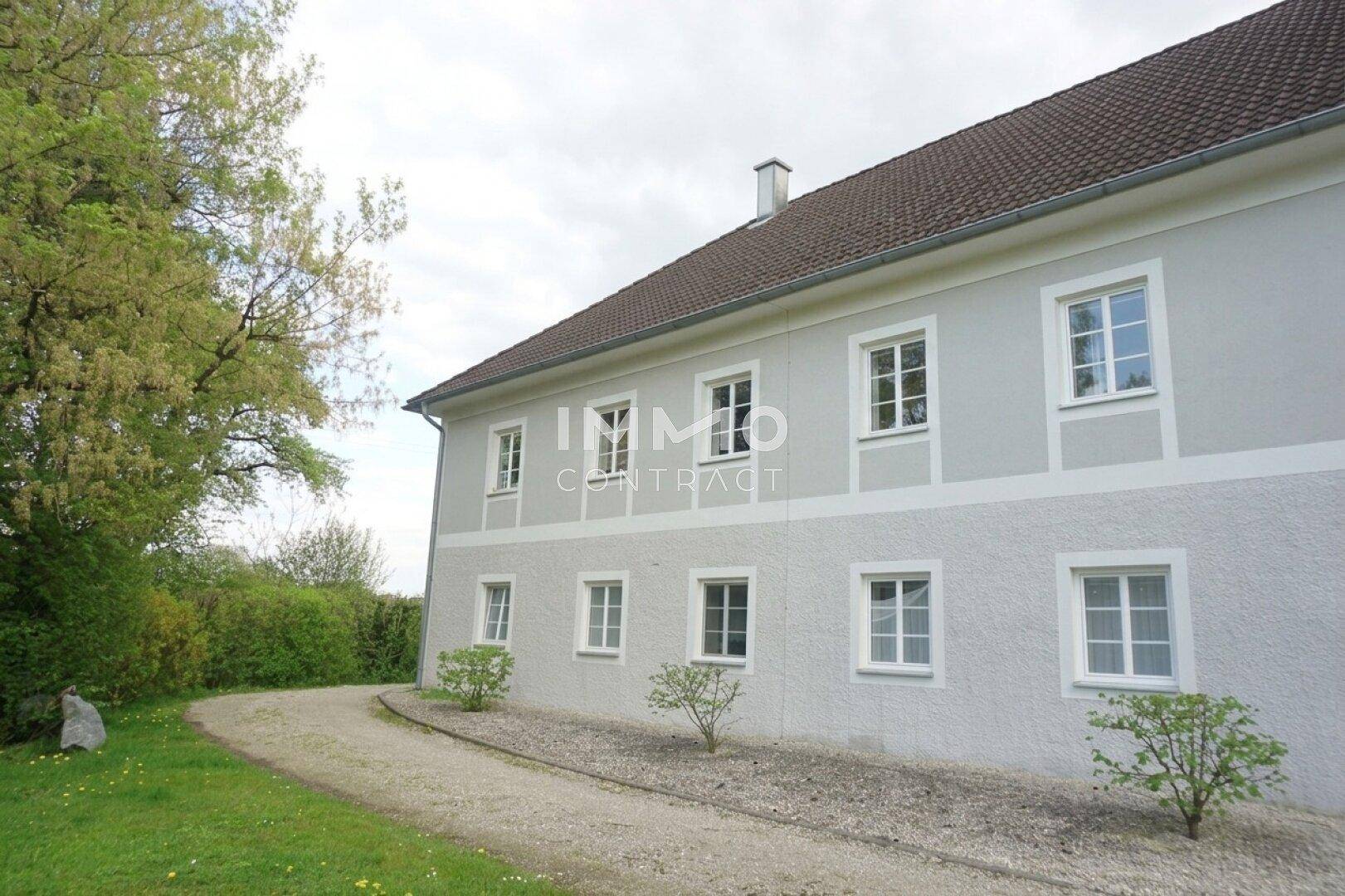 Traditionelles Gebäude mit heller Fassade, vielen Fenstern und einem geschwungenen Kiesweg.