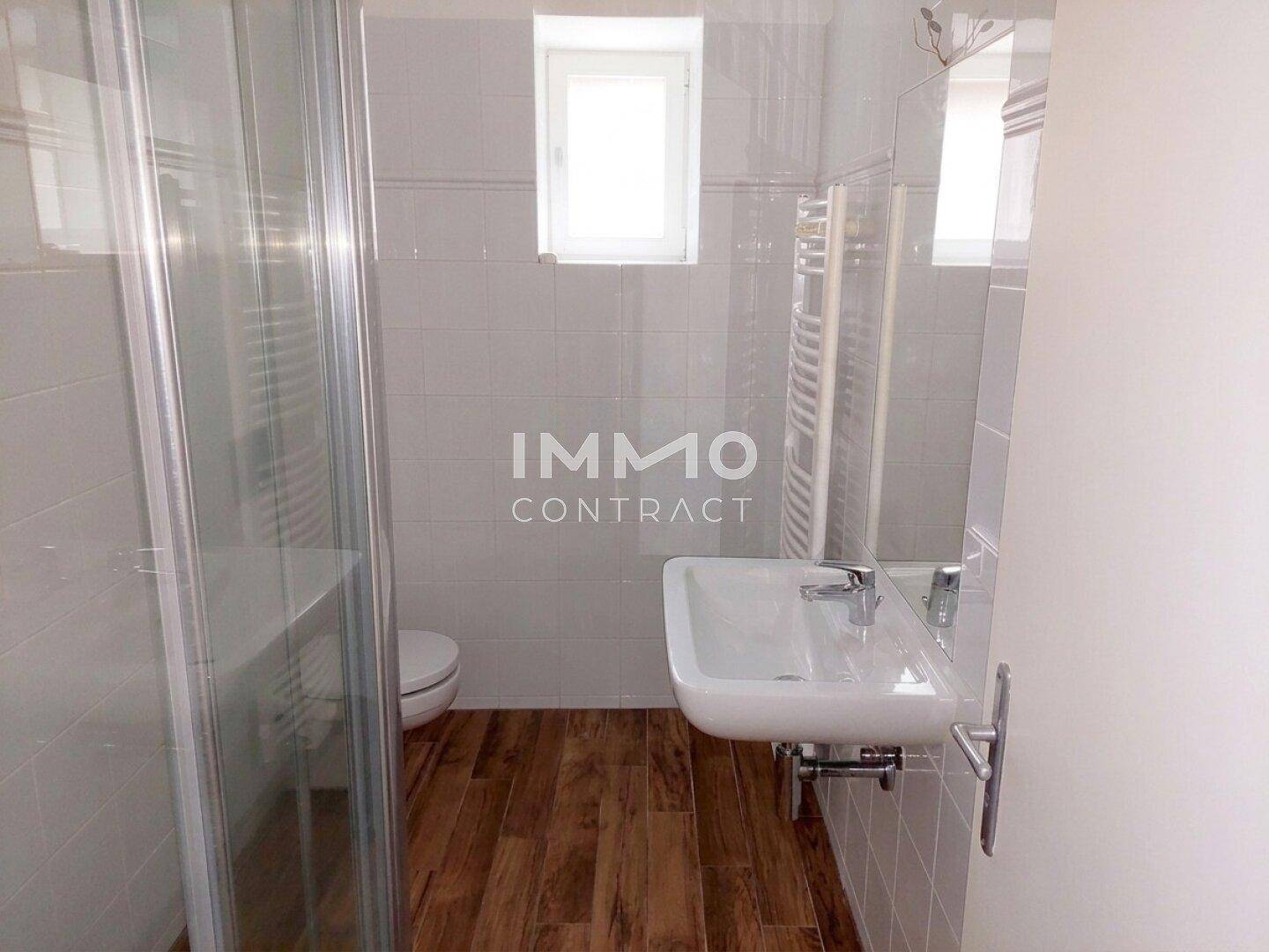 Modernes Badezimmer mit Duschkabine, Waschbecken, WC und hellen Fliesen.