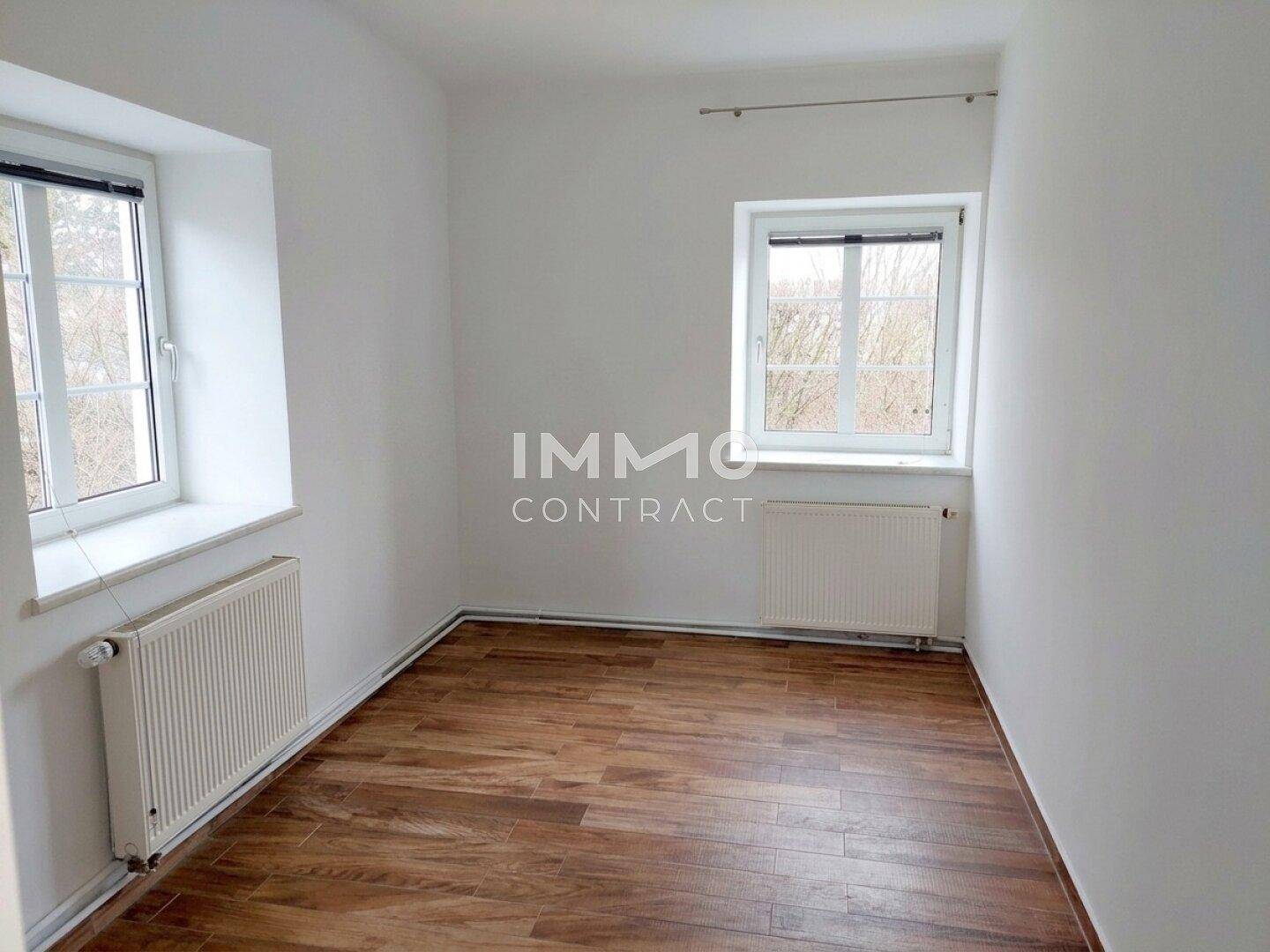 Helles Schlafzimmer mit Laminatboden, weißen Wänden und zwei Fenstern für natürliche Belichtung.