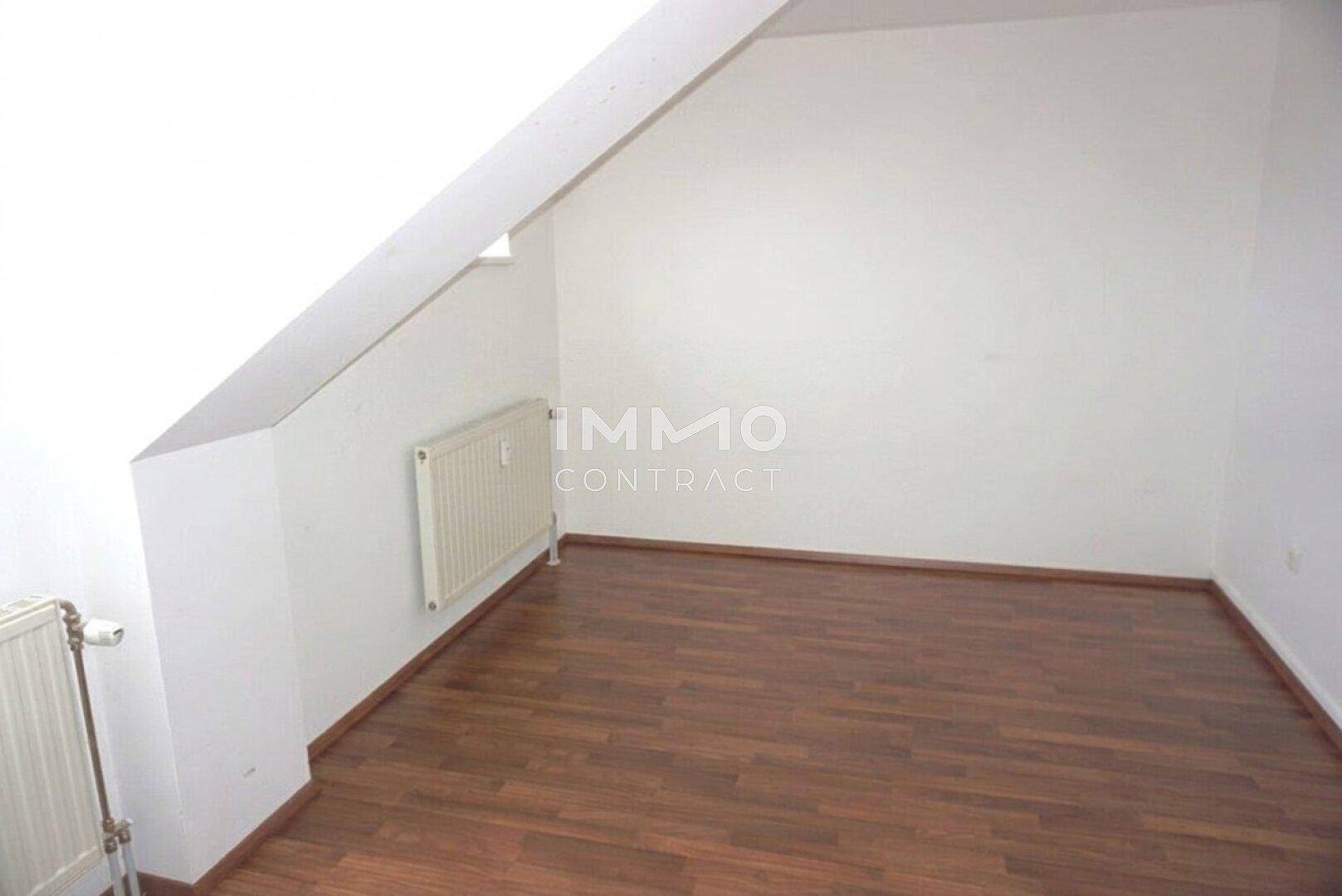 Weiteres Zimmer im Dachgeschoss mit Laminatboden, schrägen Wänden und Heizkörpern.