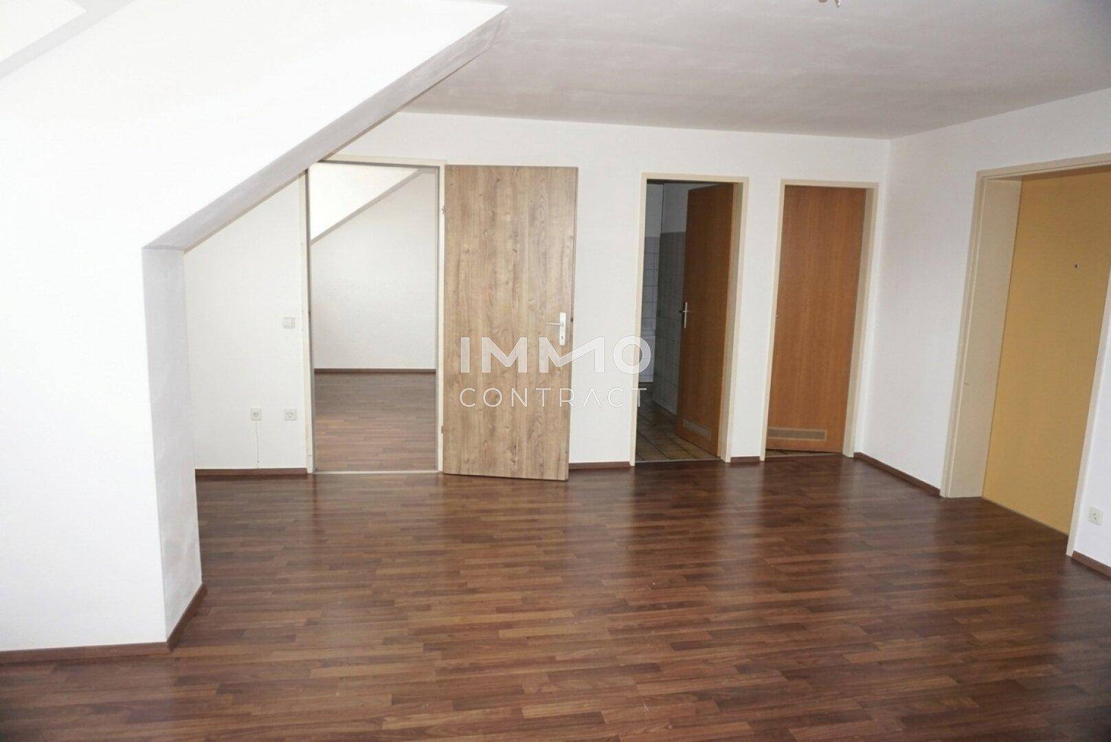 Geräumiges Zimmer im Dachgeschoss mit Laminatboden und mehreren Türöffnungen.