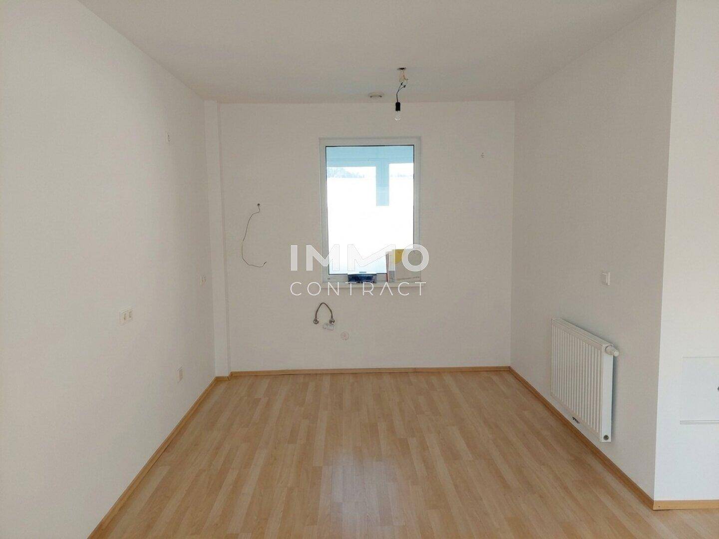 Heller, leerer Raum in gutem Zustand mit hellem Laminatboden, weißen Wänden, Fenster und Heizkörper.