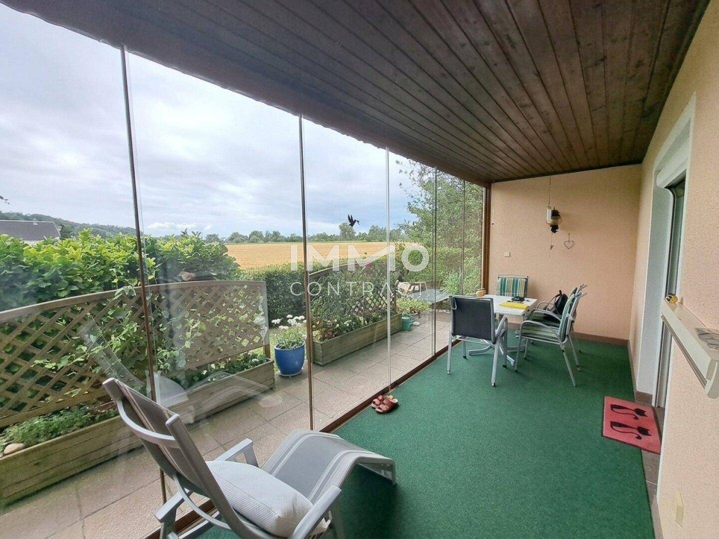 Verglaste Loggia mit Sitzgelegenheiten und weitem Blick über die umliegende Landschaft und Felder.