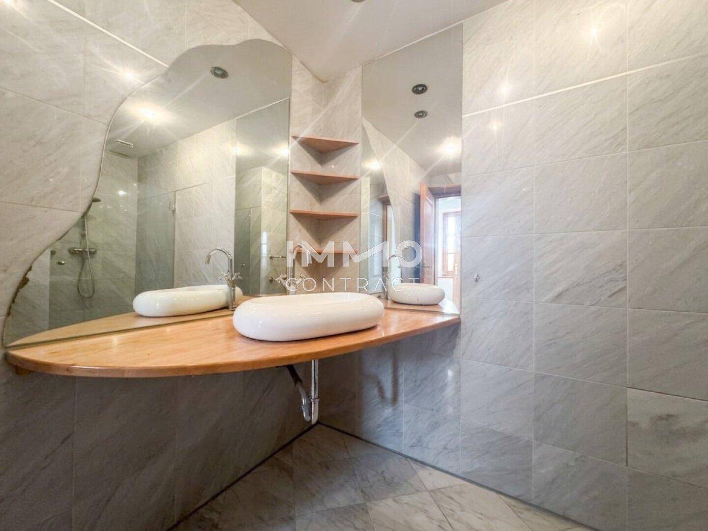 Elegantes Badezimmer mit zwei Waschbecken, Marmorfliesen und einem großen, geschwungenen Spiegel.