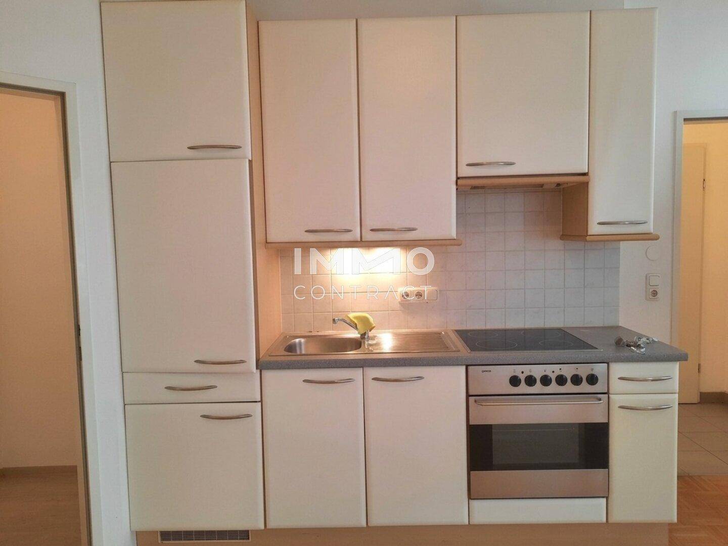 Kompakte Küchenzeile mit weißen Schränken, Spüle, Herd und Backofen in hellem Design.