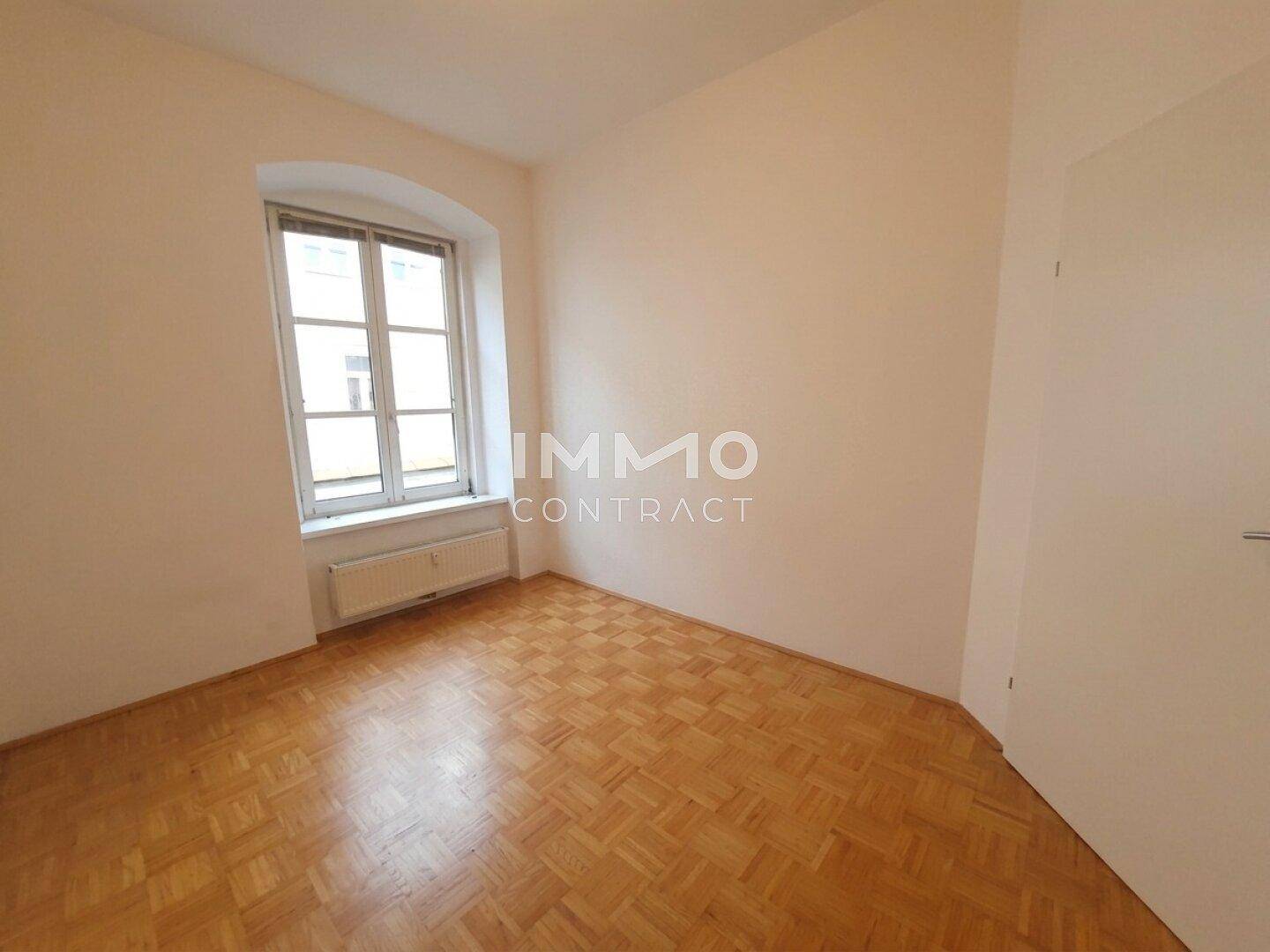 Helles Schlafzimmer mit Parkettboden und einem großen Fenster, unmöbliert und bezugsfertig.