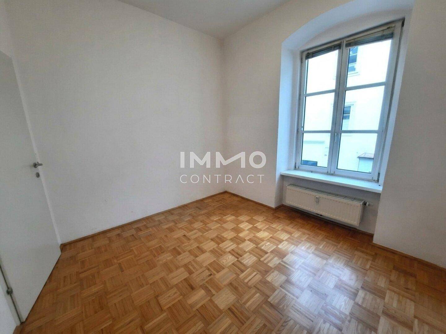 Unmöbliertes Zimmer mit Parkettboden und einem großen Fenster, ideal als Schlaf- oder Arbeitszimmer.