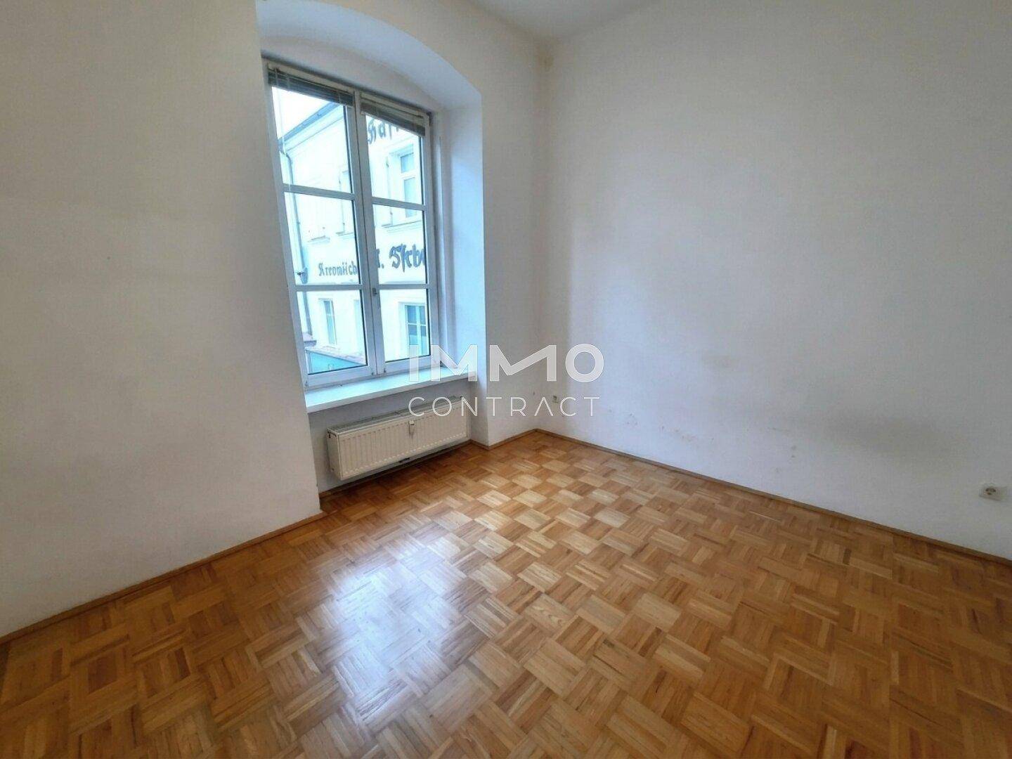 Leeres Zimmer mit Parkettboden und einem Fenster, das einen Blick auf die Umgebung bietet.