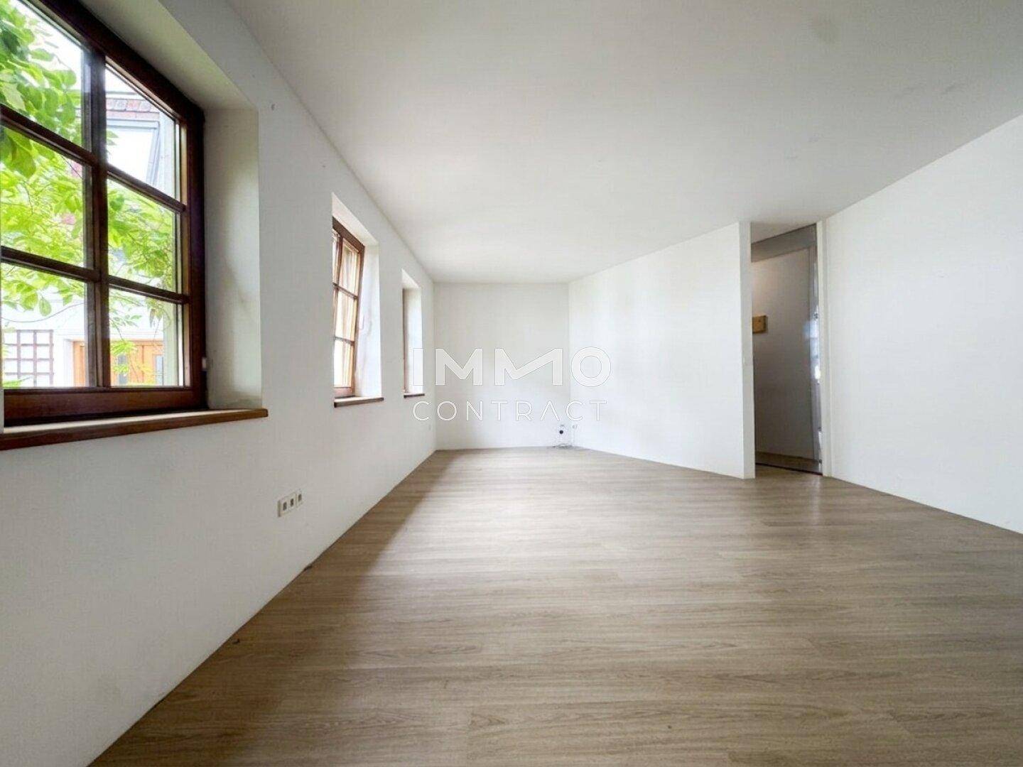 Geräumiger, heller Raum mit Laminatboden und großen Fenstern, ideal für Wohn- oder Essbereich.