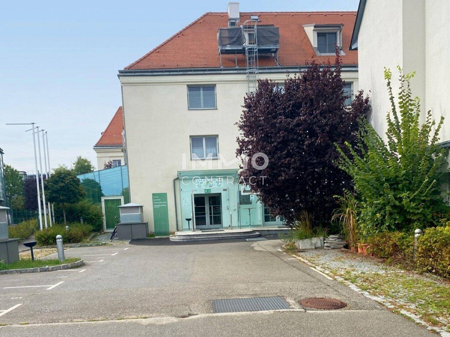 Außenansicht des Gebäudes mit Parkplätzen und moderner Glasfassade am Eingangsbereich.