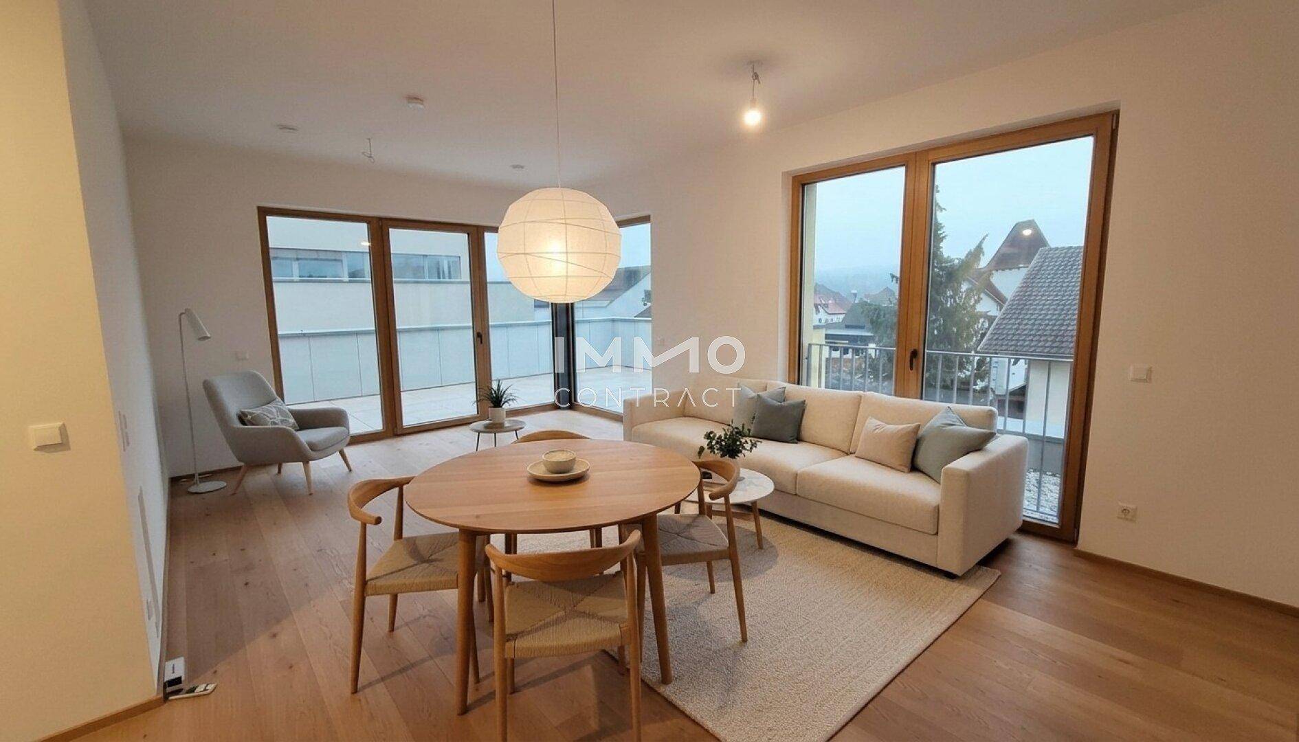 Heller offener Wohn-Essbereich mit Holzboden, großen Fenstern und Zugang zu einem Balkon.