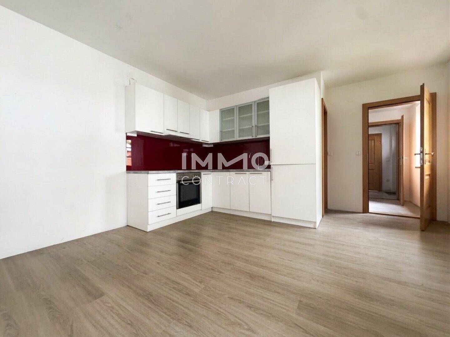 Moderne Einbauküche mit weißen Schränken, roter Rückwand und integriertem Backofen in hellem Raum.
