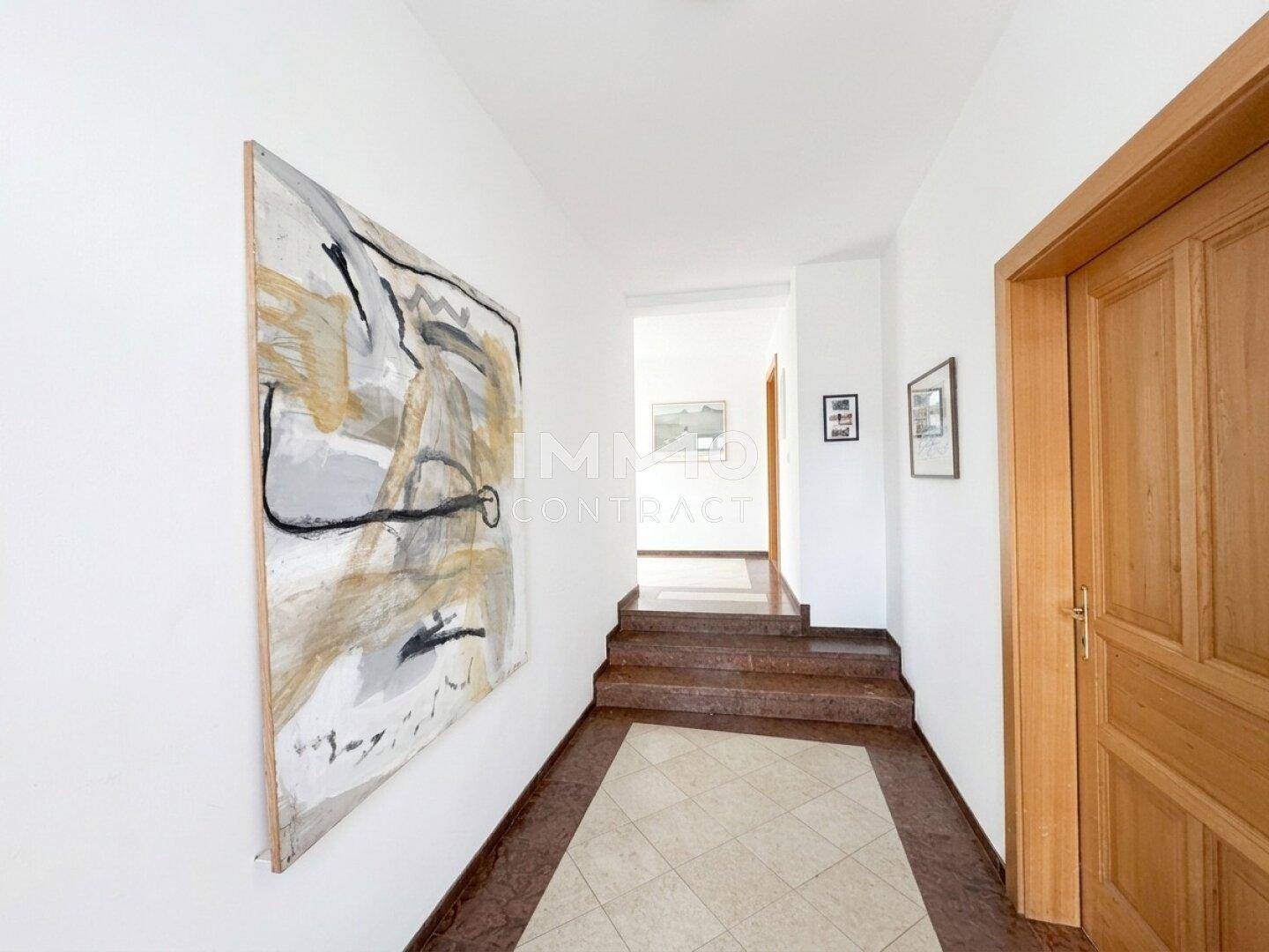 Geräumiger Flur mit Treppe, Kunstwerk an der Wand und Fliesenboden in warmen Tönen.
