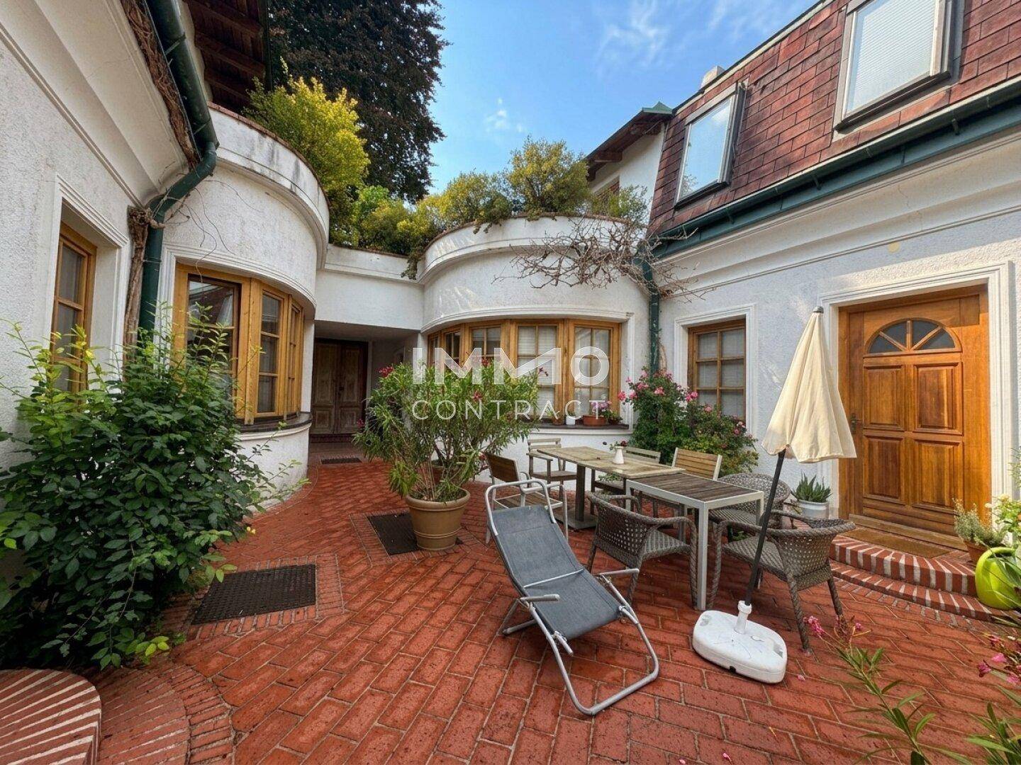 Sonniger Innenhof mit gepflastertem Bereich, Gartenmöbeln und üppiger Bepflanzung.
