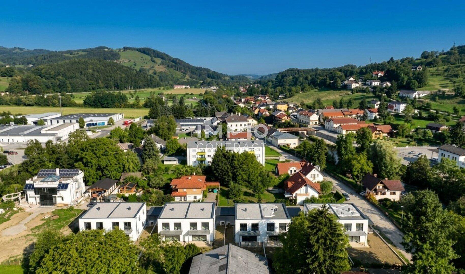 Luftaufnahme einer modernen Wohnsiedlung mit Neubauten, eingebettet in eine grüne Hügellandschaft.