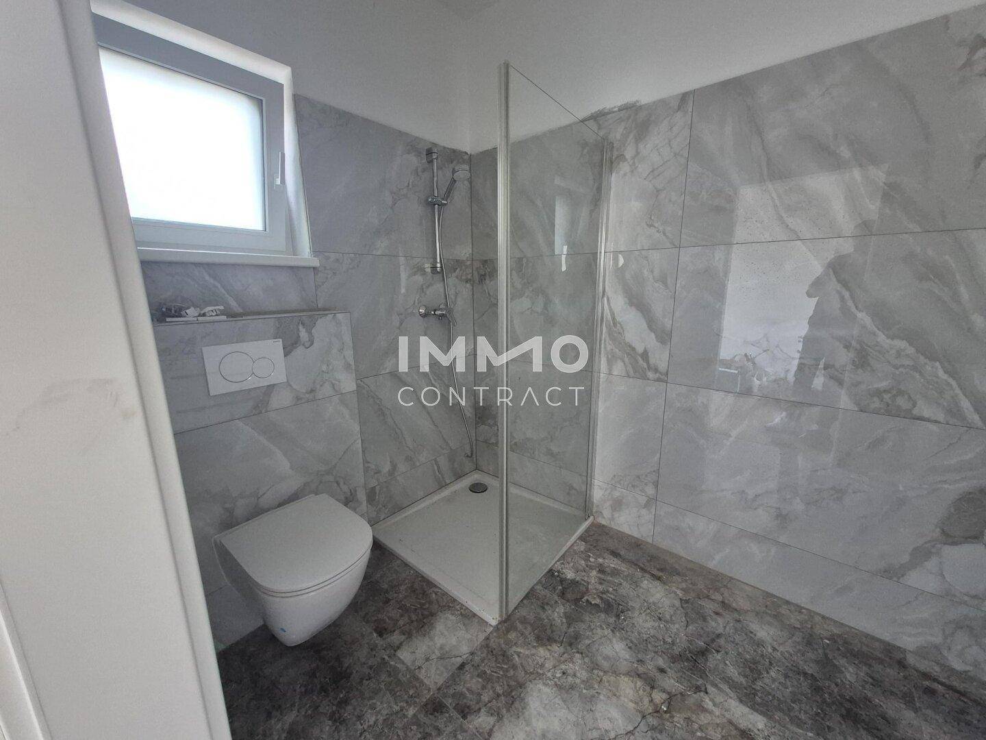 Modernes Badezimmer mit grauen Marmorfliesen, wandhängendem WC und begehbarer Dusche.