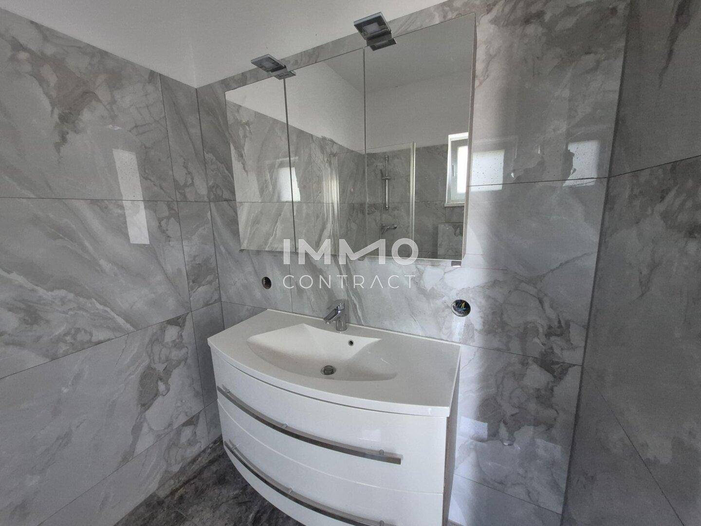 Modernes Badezimmer mit Marmorfliesen, elegantem Waschtisch und Spiegelschrank.