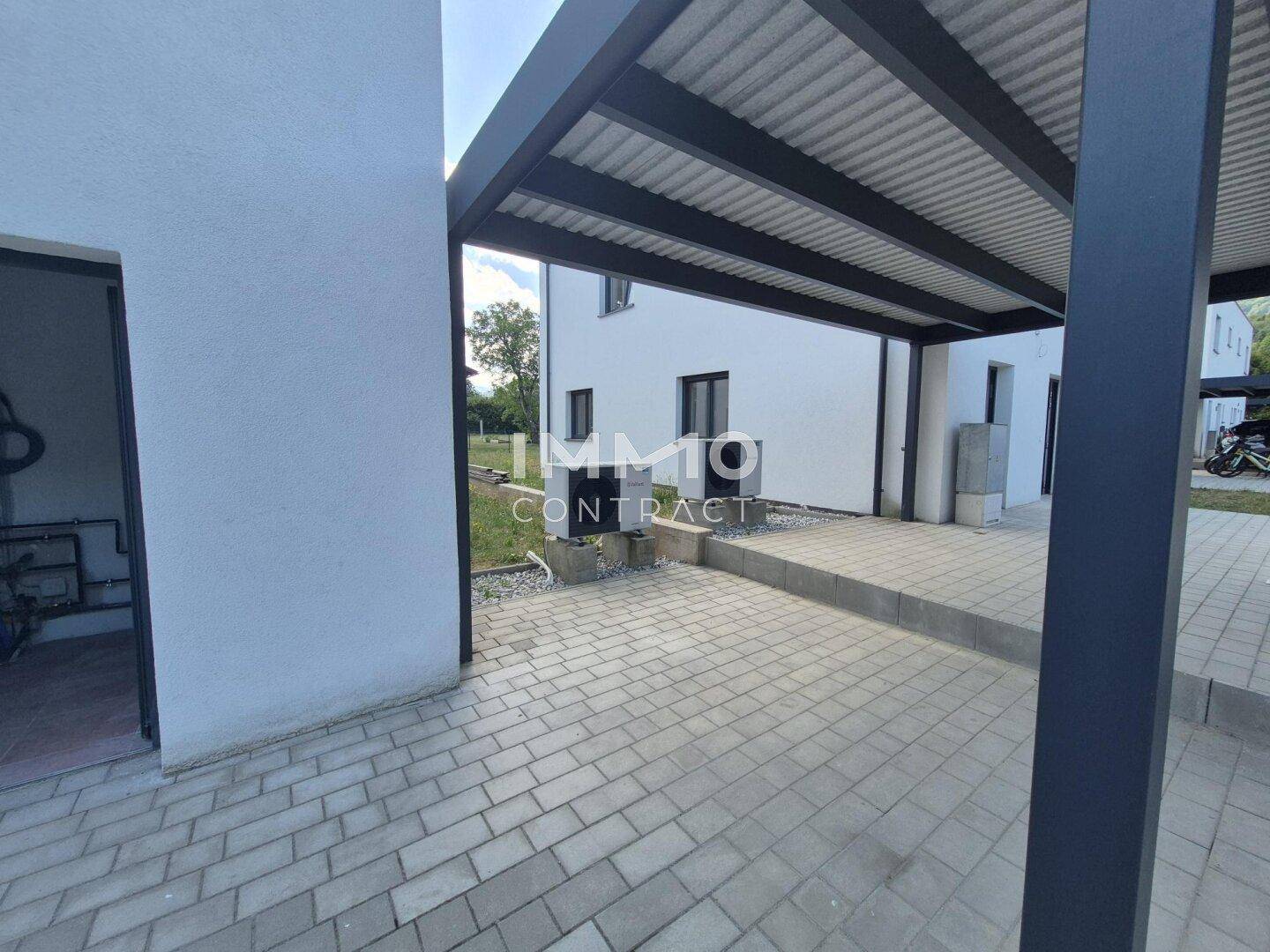 Überdachter Parkplatz mit Pflastersteinen neben dem modernen Wohngebäude.