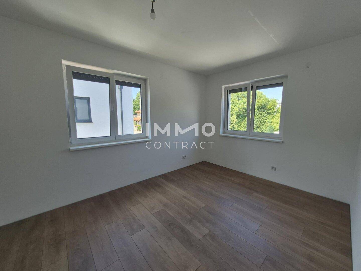 Helles Schlafzimmer mit Laminatboden und zwei Fenstern, die viel Tageslicht bieten.