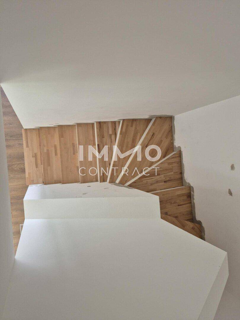 Moderne Treppe mit Holzstufen und weißen Setzstufen, die die verschiedenen Ebenen verbindet.