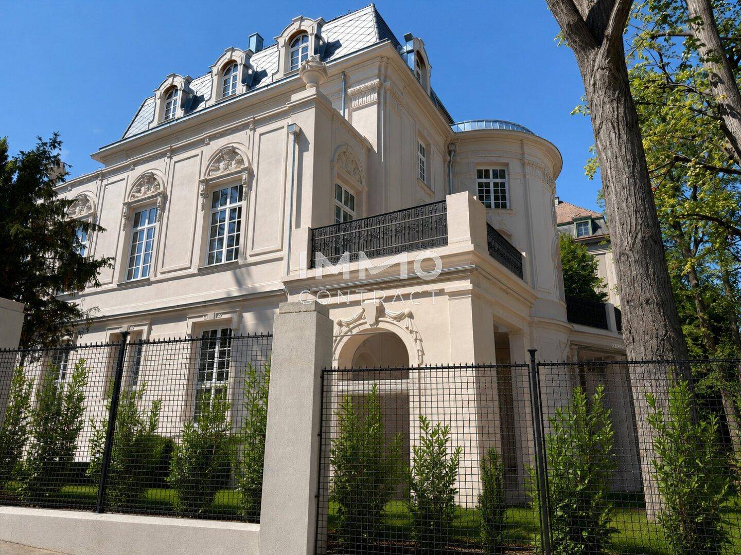 Seitenansicht der eleganten Villa mit schmiedeeisernem Zaun und gepflegter Gartenanlage.