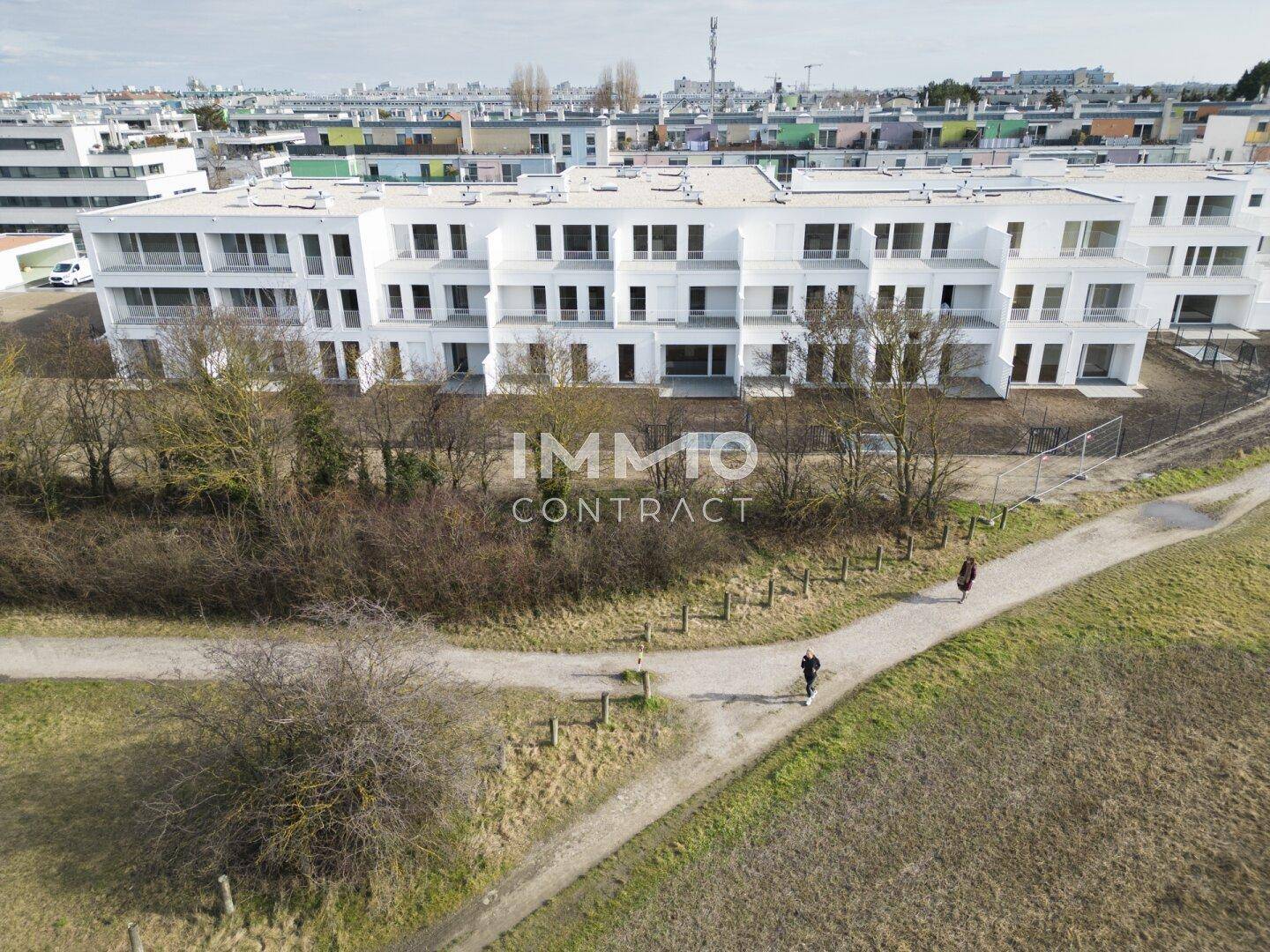 Moderne Wohngebäude in einer Siedlung mit Wegen und Grünflächen, umgeben von weiteren Neubauten.