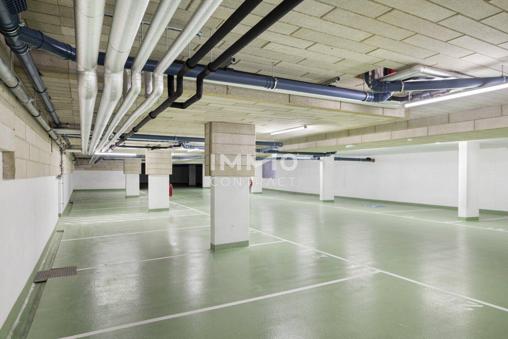 Geräumige Tiefgarage mit markierten Stellplätzen und sichtbaren Versorgungsleitungen an der Decke.