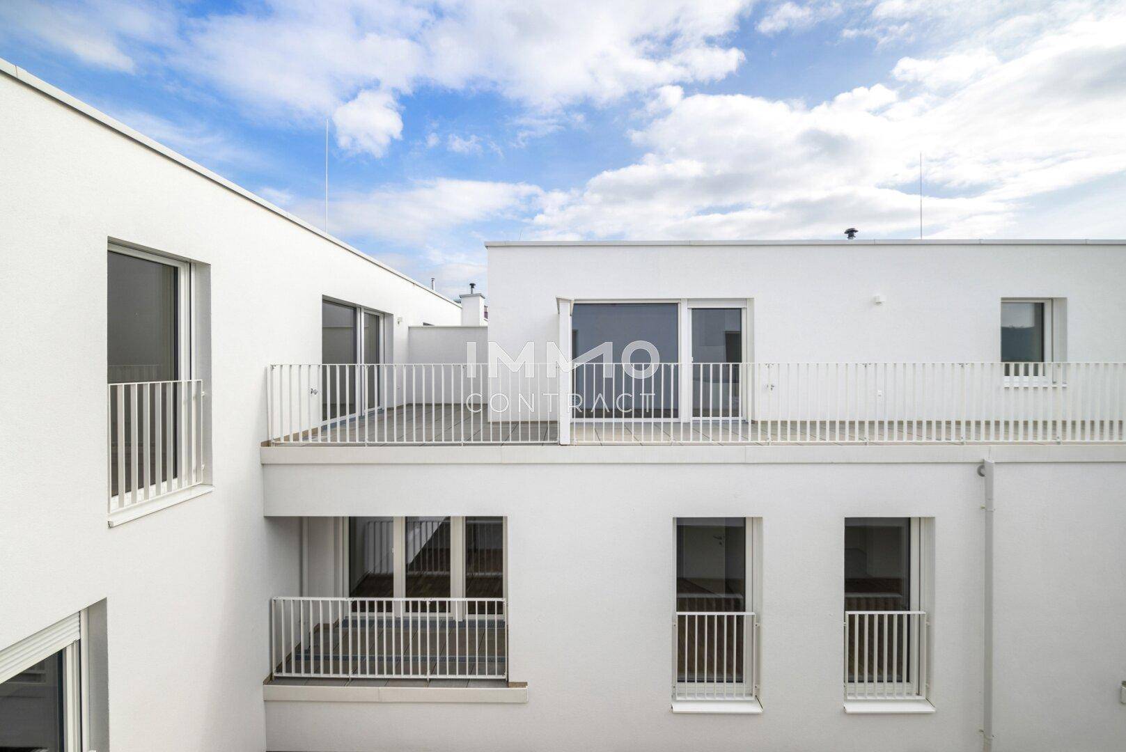 Moderne weiße Fassade eines Neubaus mit mehreren Balkonen und großen Fenstern.