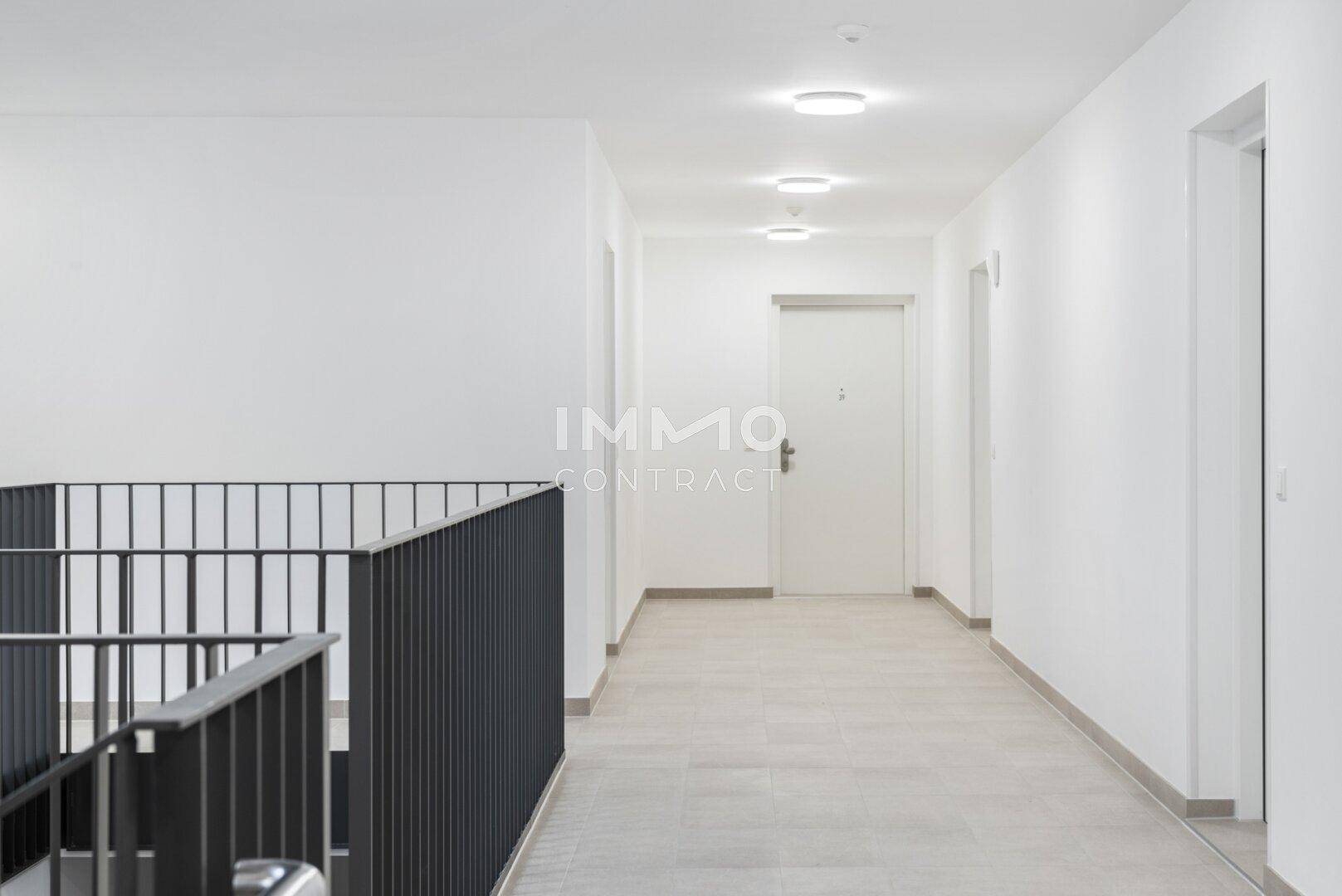 Heller Flur in einem modernen Gebäude mit weißen Wänden und hellgrauem Fliesenboden.