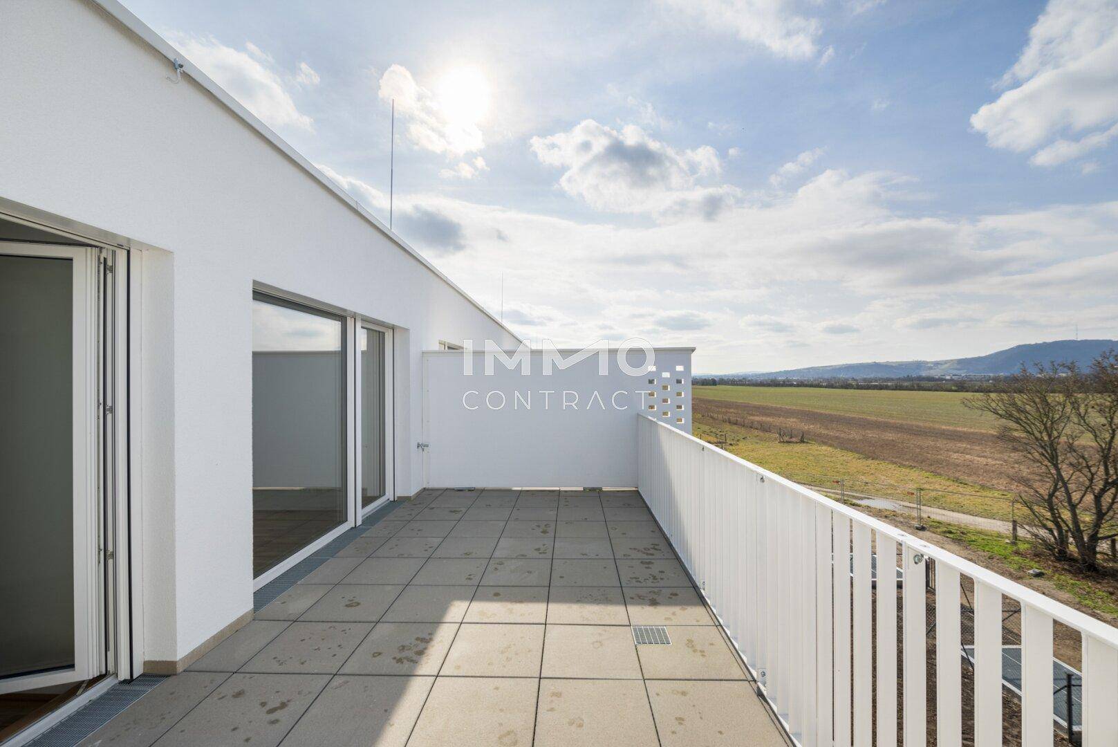 Sonniger Balkon mit Fliesenboden und Zugang zu Innenräumen, bietet einen weiten Landschaftsblick.