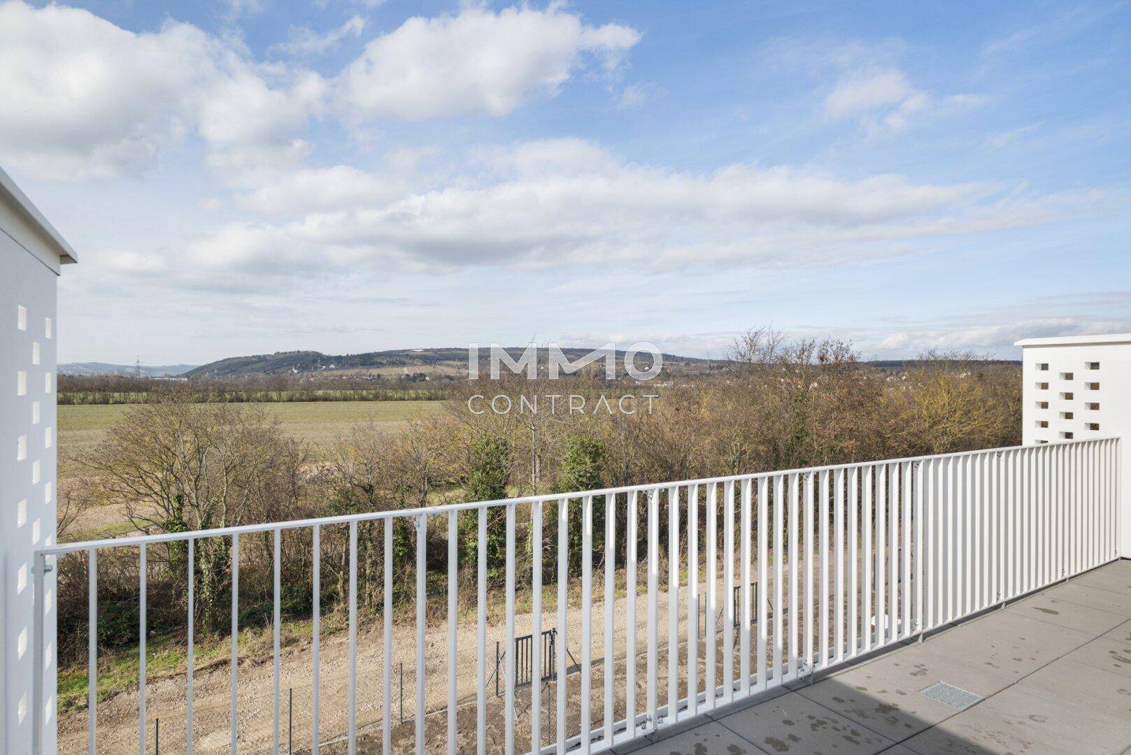 Balkon mit weißem Geländer und weitem, unverbautem Blick über Felder und eine hügelige Landschaft.