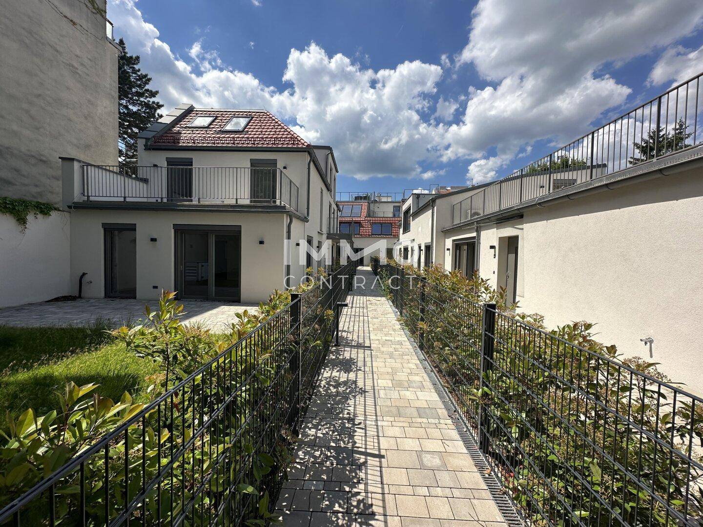 Gepflasterter Weg durch einen gepflegten Gartenbereich zwischen den Gebäuden, einladend und grün.