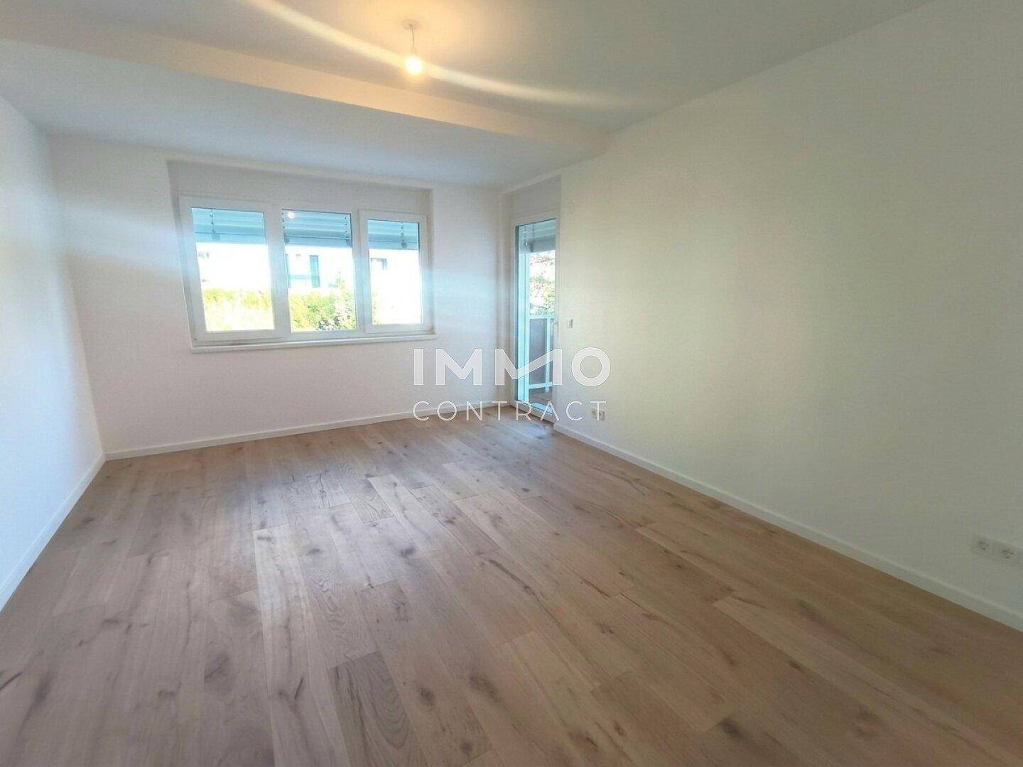Heller, leerer Raum mit modernem Holzboden und Zugang zu einem sonnigen Außenbereich.
