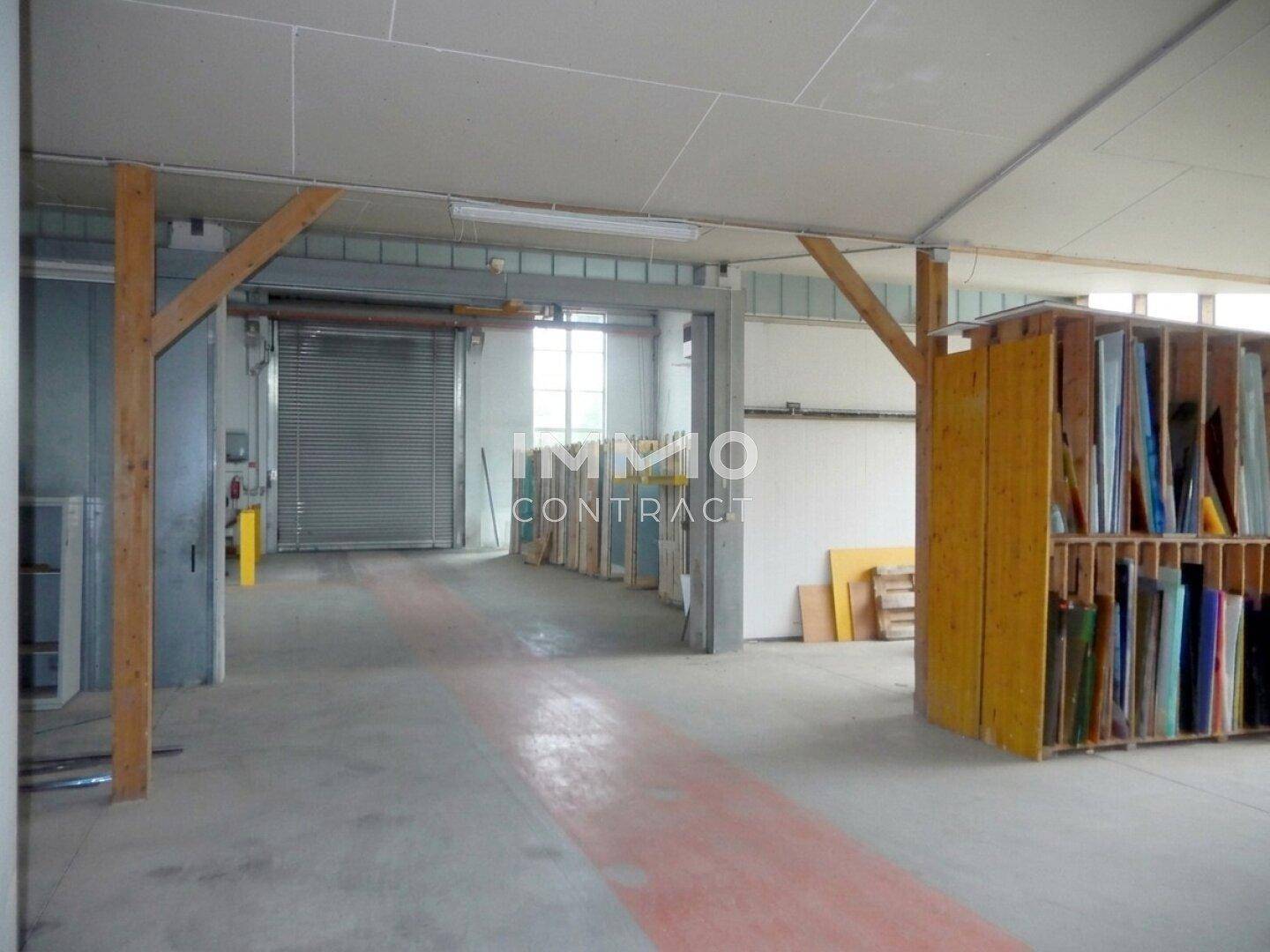 Innenbereich mit Holzstützbalken und einer Rolltoröffnung im Hintergrund, geeignet als Lager- oder Arbeitsbereich.