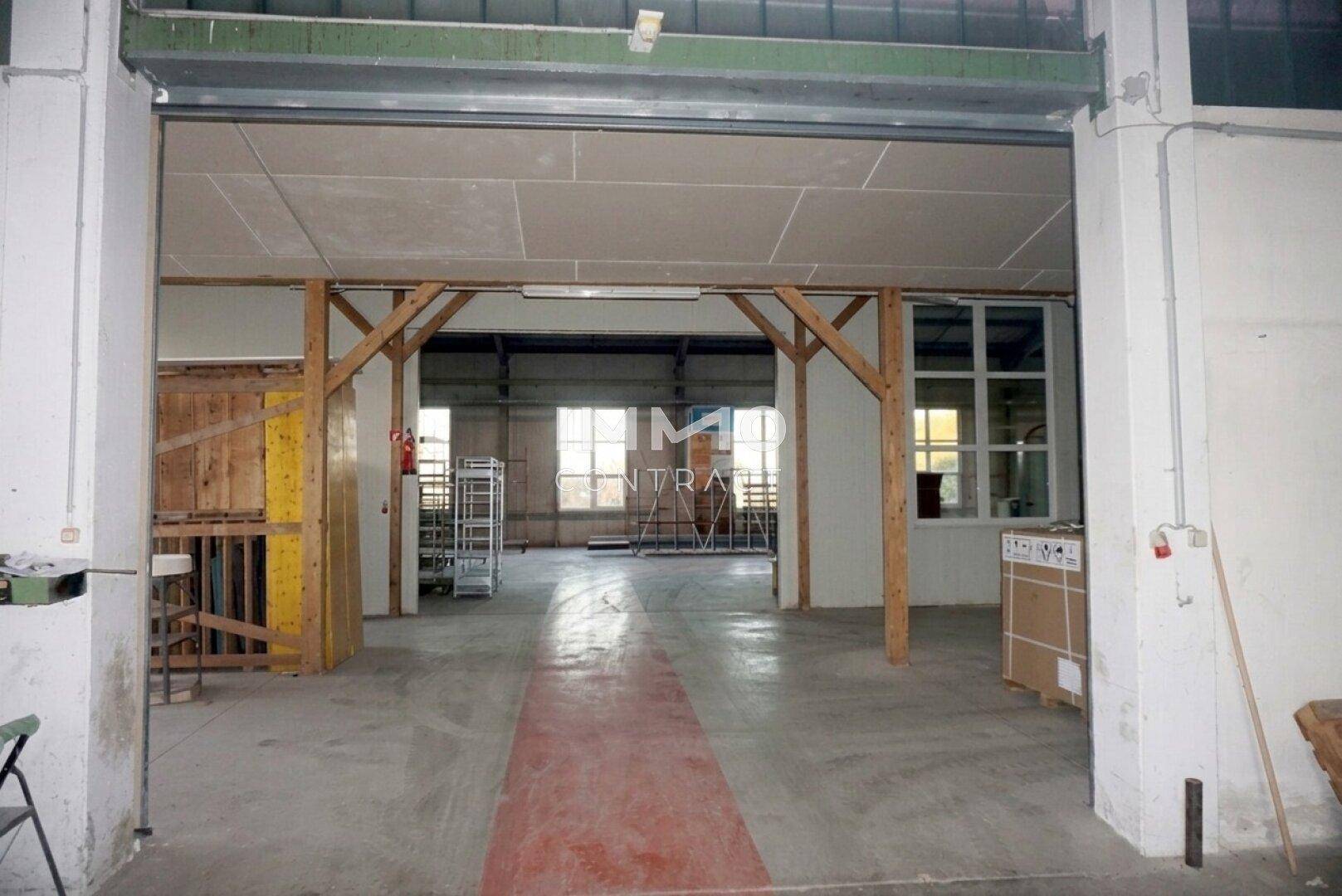 Blick durch eine Öffnung in eine geräumige Industriehalle mit Betonboden und hohen Decken im Hintergrund.