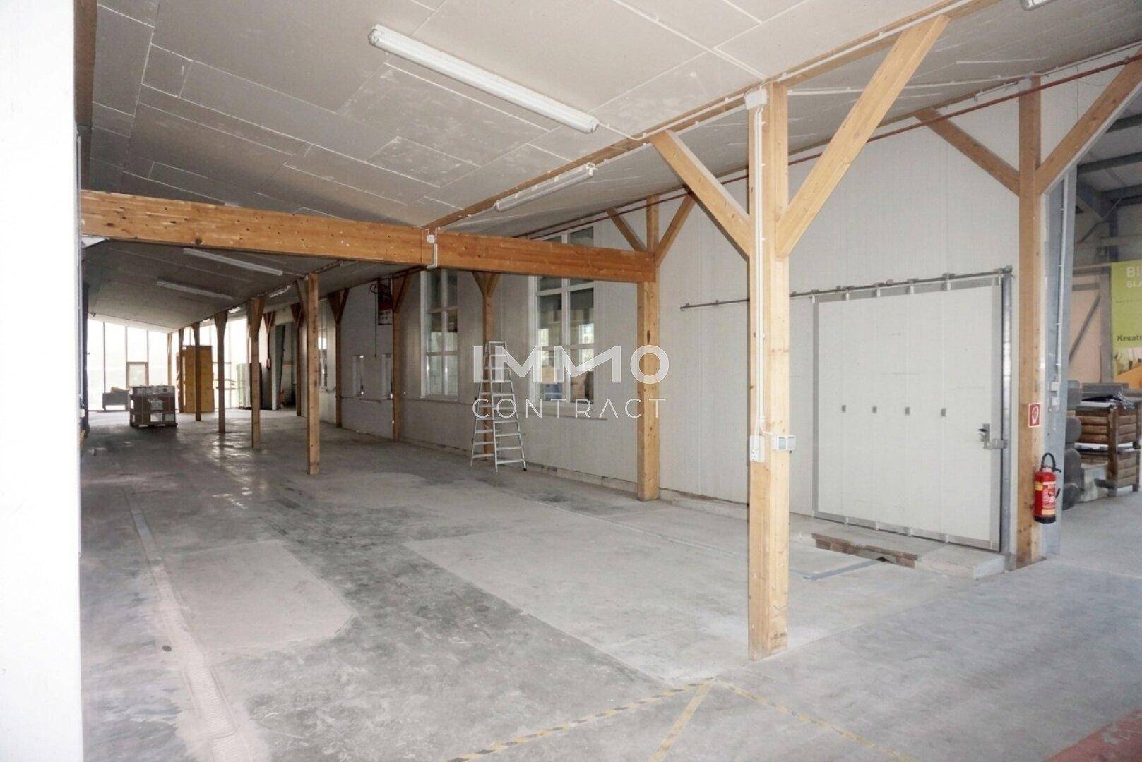 Langer Hallenbereich mit Holzstützen, Betonboden und einem Rolltor, gut geeignet für industrielle Nutzung.
