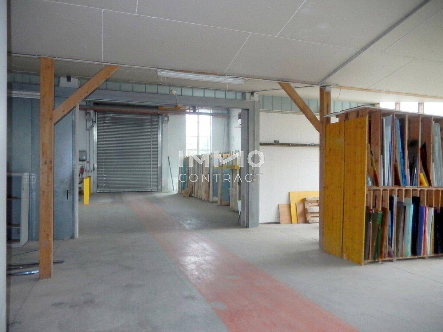 Innenbereich einer Halle mit Rolltor, Holzstützen und Betonboden, ideal für Lagerung oder Werkstatt.