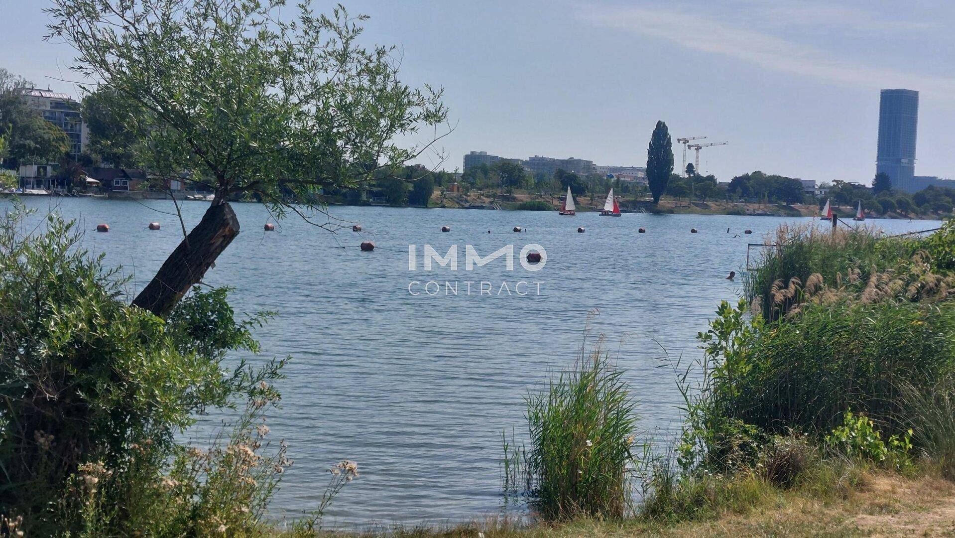 Panoramablick auf einen See mit Segelbooten und einer modernen Hochhausarchitektur am Horizont.