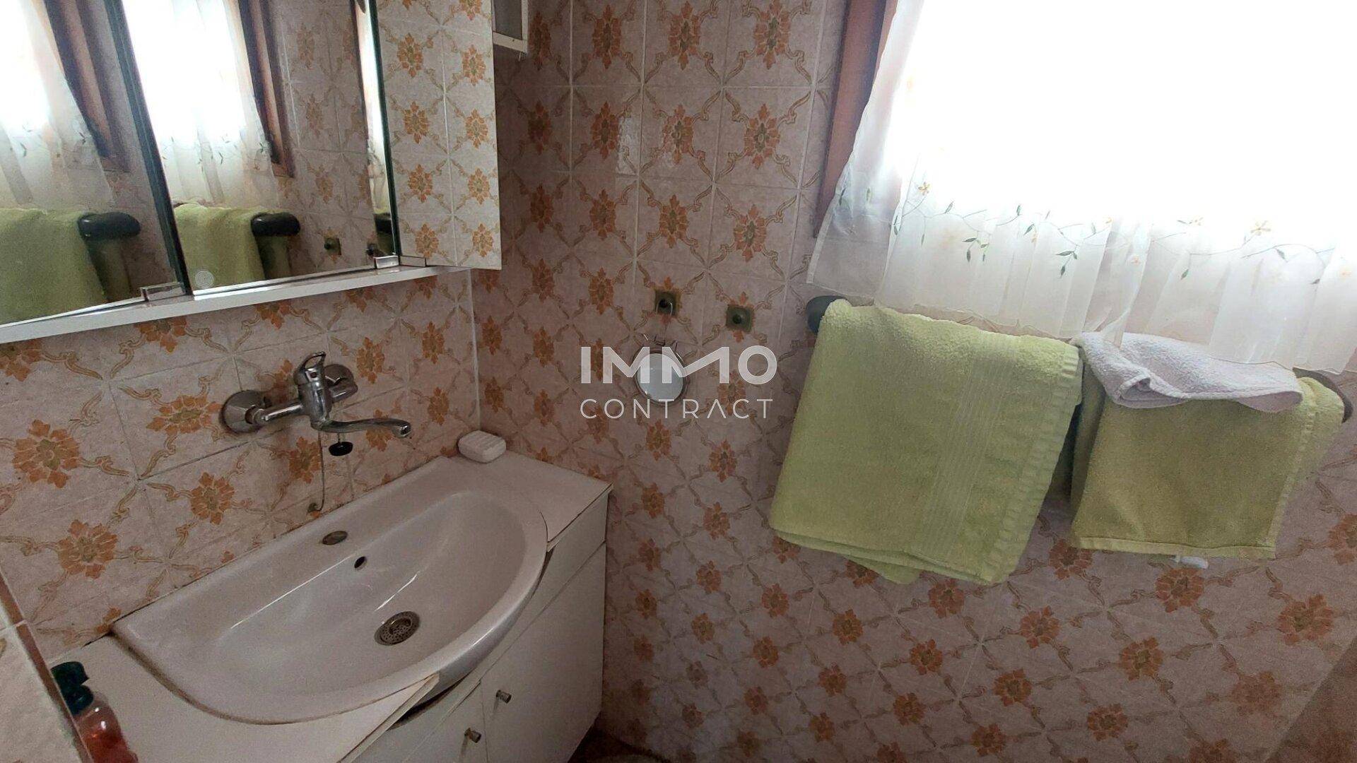 Badezimmer mit Waschbecken, Spiegelschrank und floral gemusterten Wandfliesen.