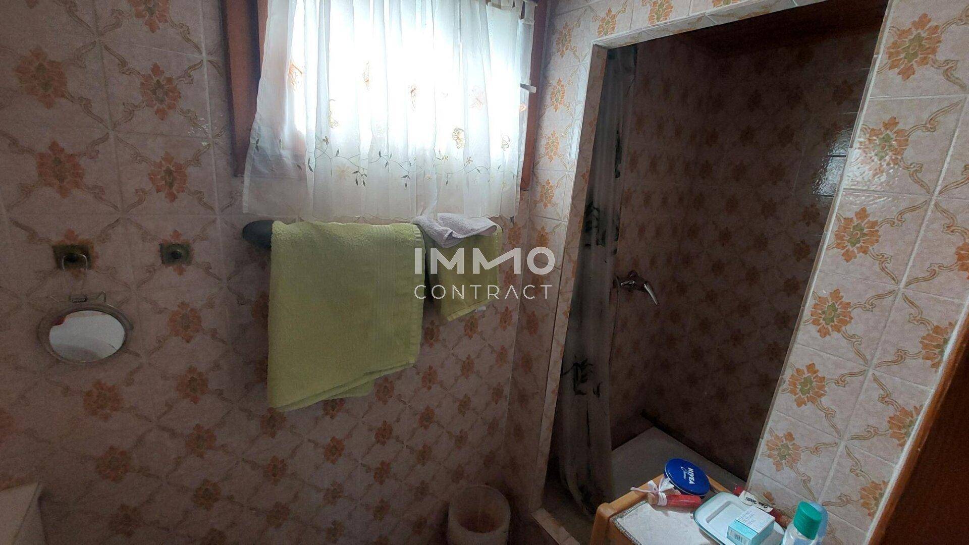 Badezimmer mit floral gemusterten Fliesen, einem Fenster und einer einfachen Duschkabine.