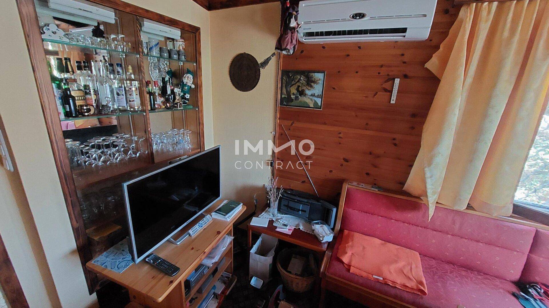 Gemütliches Wohnzimmer mit Holzwänden, einem Vitrinenschrank, Fernseher und Klimaanlage.