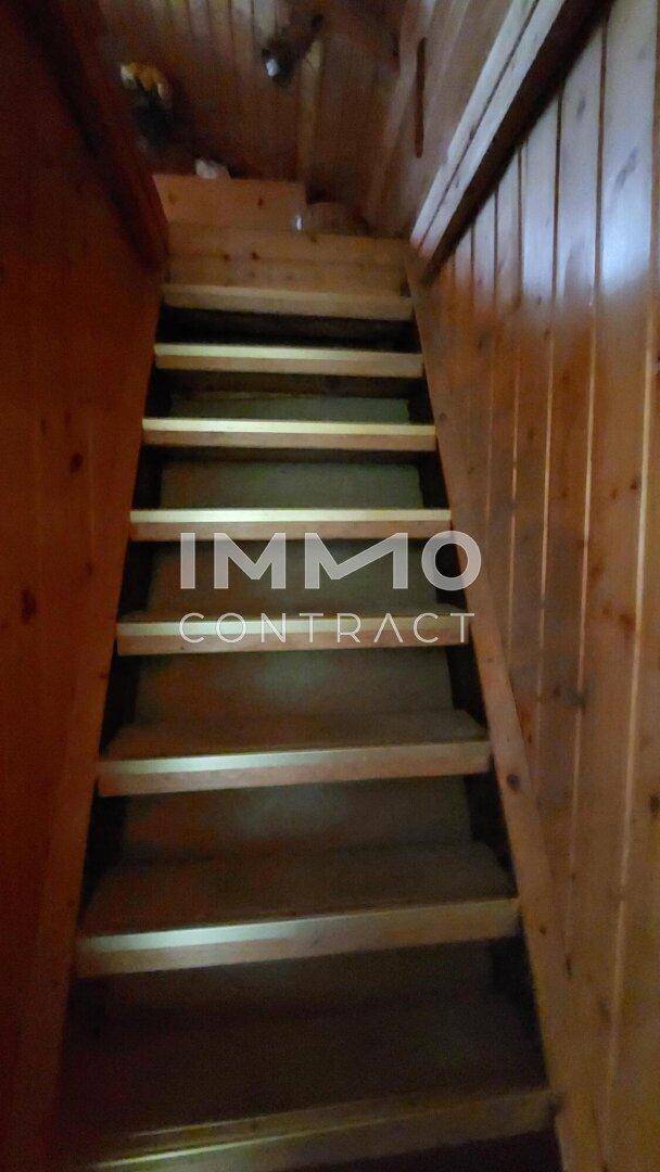 Einfache Holztreppe führt in ein oberes Stockwerk, umgeben von Holzvertäfelung.