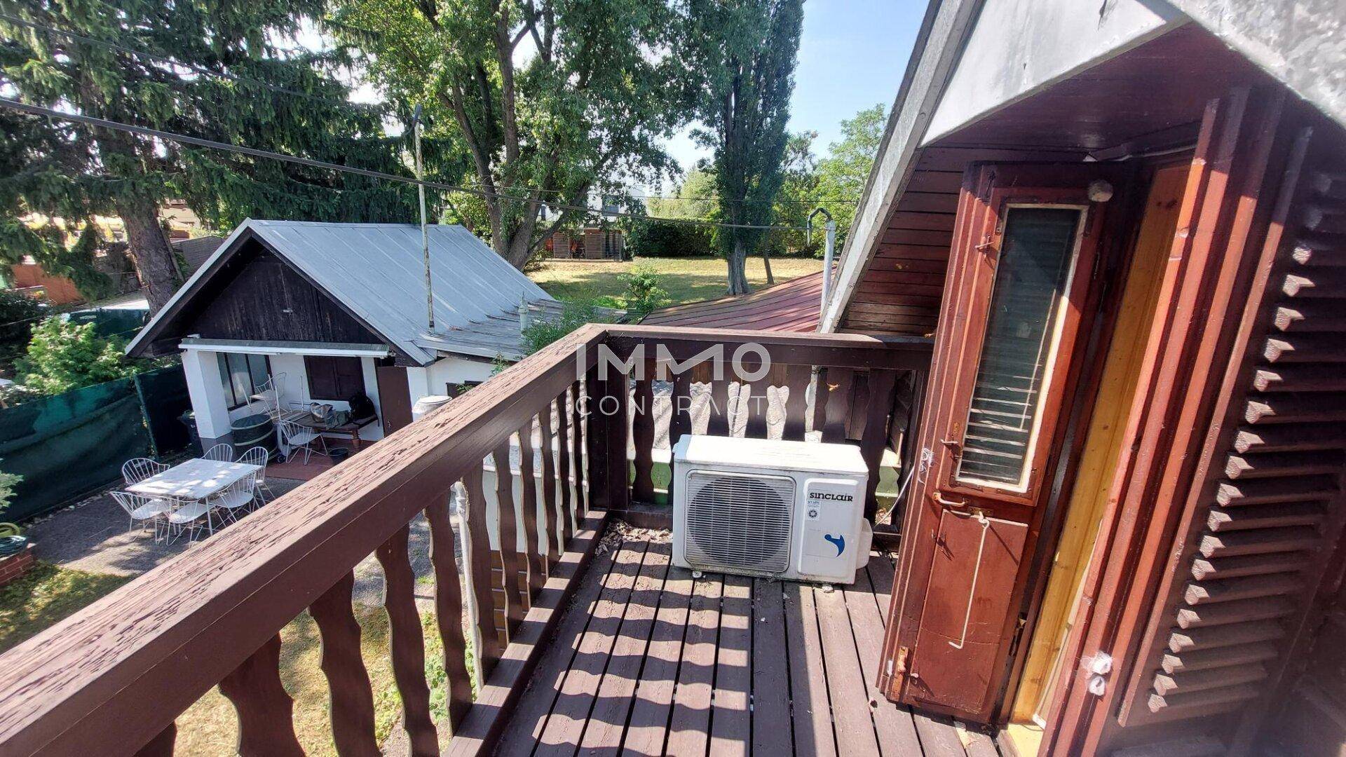 Gemütlicher Holzbalkon mit Klimaanlage und Ausblick auf ein weiteres kleines Haus und viel Grün.